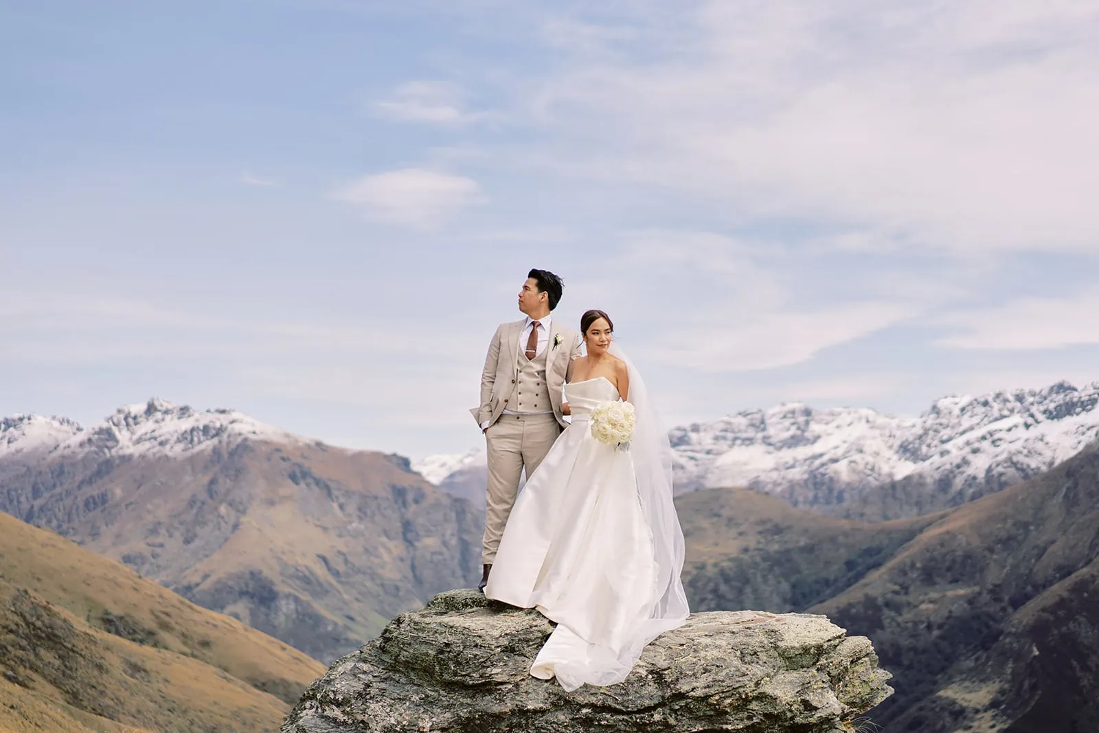 Queenstown Elopement Heli Wedding Photographer クイーンズタウン結婚式 | A man and woman standing on a rock with mountains in the background in Queenstown.