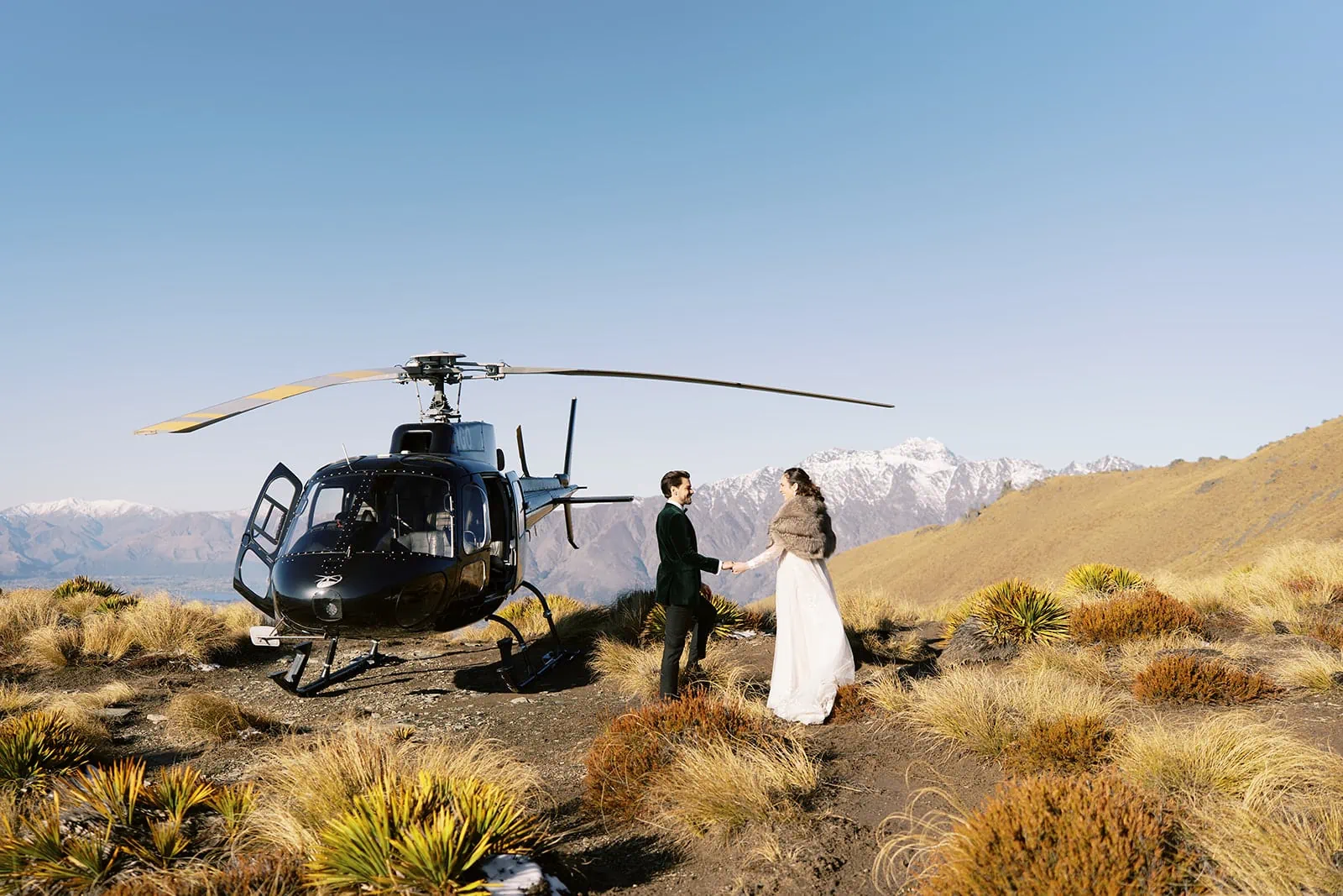 Queenstown Wedding Photographer Nat & Tim, a bride and groom, elegantly pose in front of a helicopter at Deer Park Heights in Queenstown for their memorable EloPedding wedding.