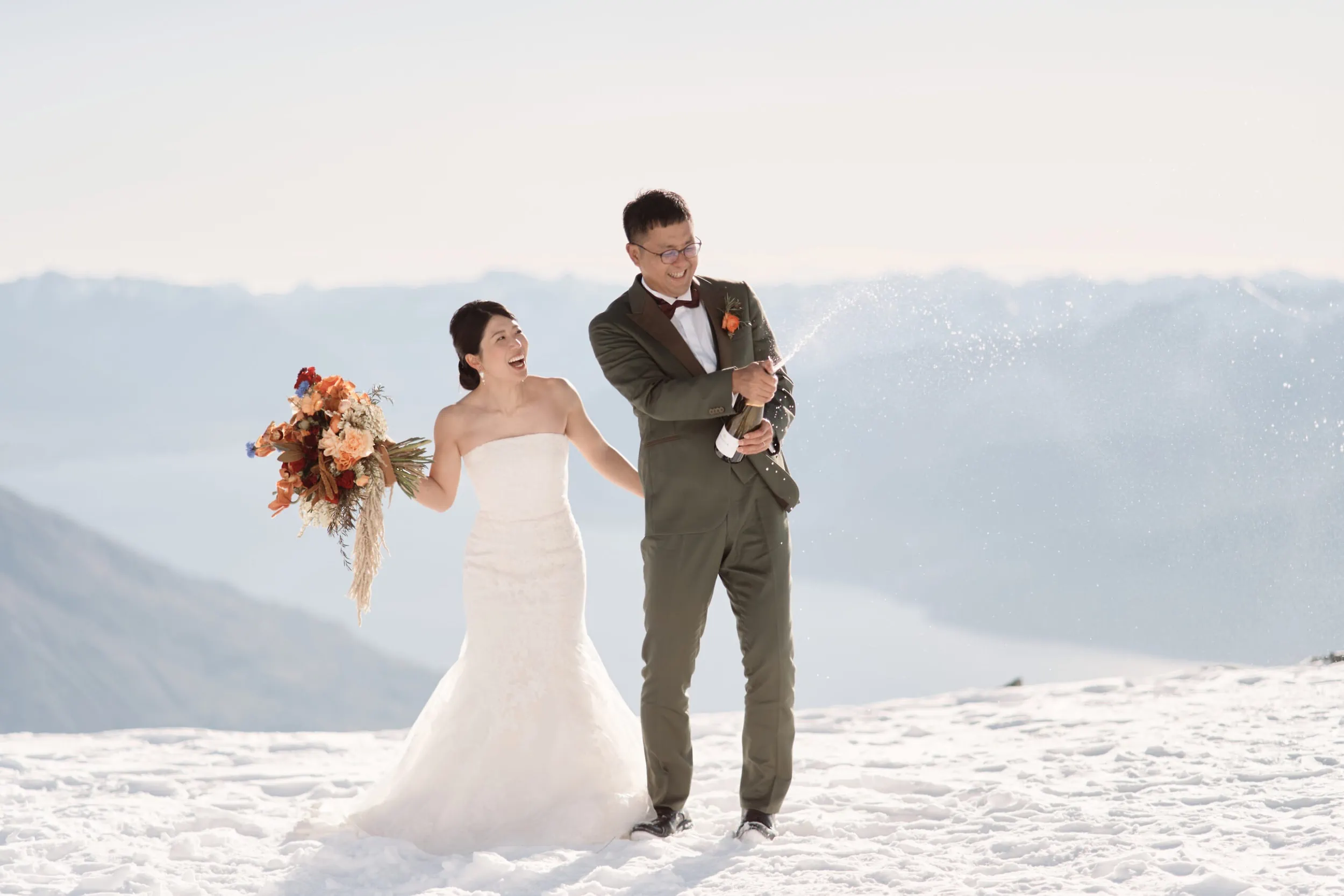 Queenstown Wedding Photographer Asumi and Atsushi, a beautiful bride and groom, embark on an extraordinary Queenstown Heli Pre Wedding Shoot. They stand gracefully atop a majestic snow-covered mountain, surrounded by