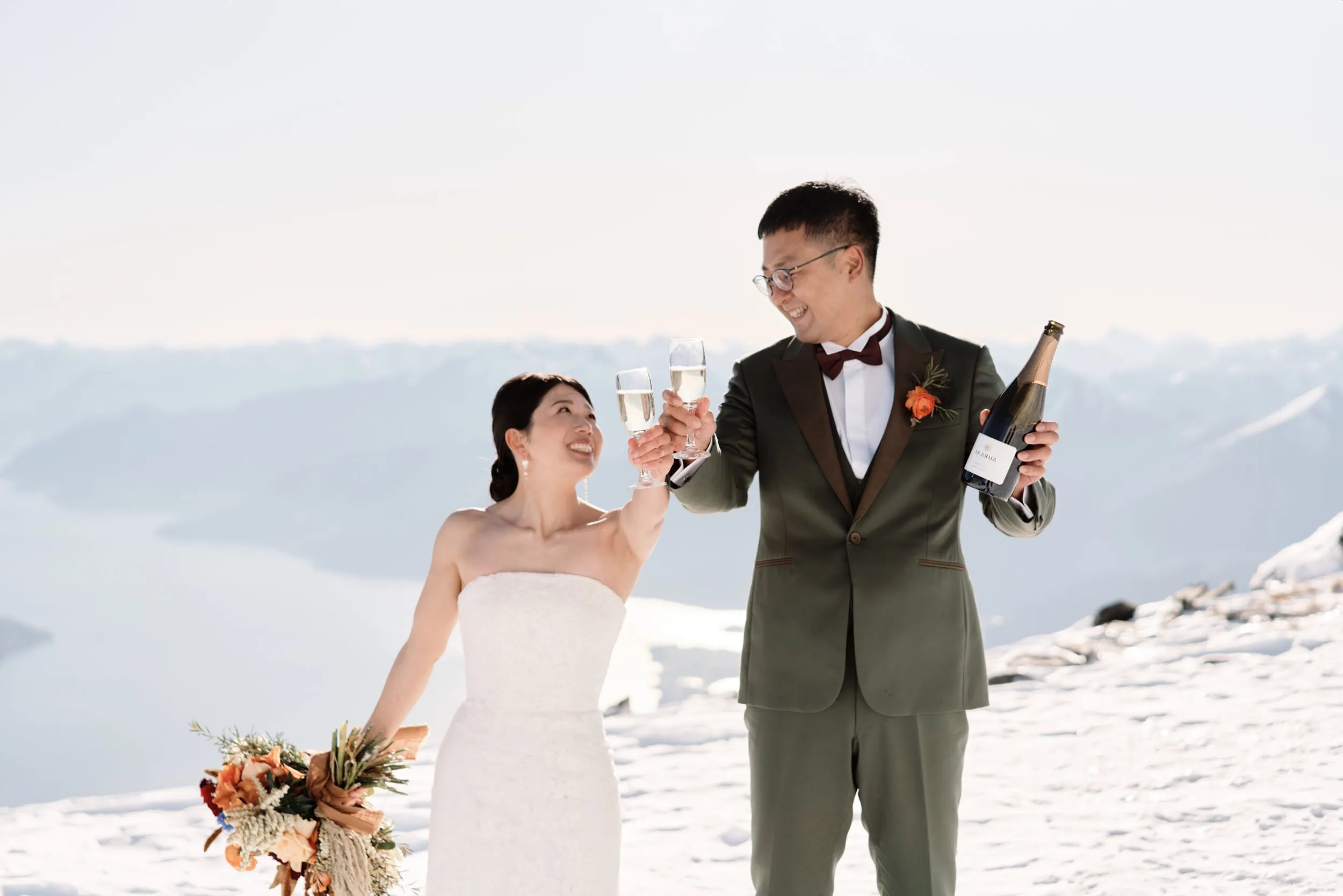Queenstown Wedding Photographer Asumi and Atsushi toasting champagne on top of a snowy mountain during their Queenstown Heli Pre Wedding Shoot.
