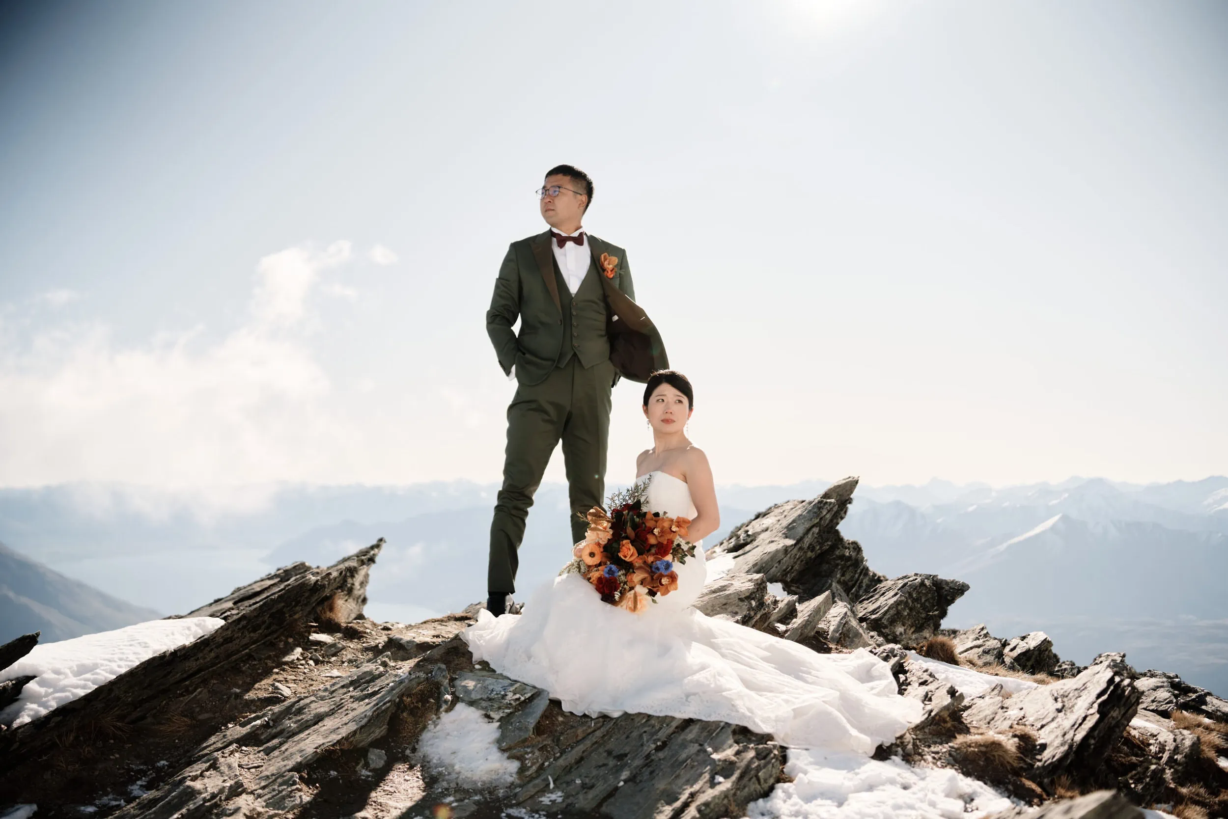 Queenstown Wedding Photographer Asumi & Atsushi, a bride and groom, embarking on a breathtaking Heli Pre Wedding Shoot in Queenstown, standing triumphantly on top of a mountain.