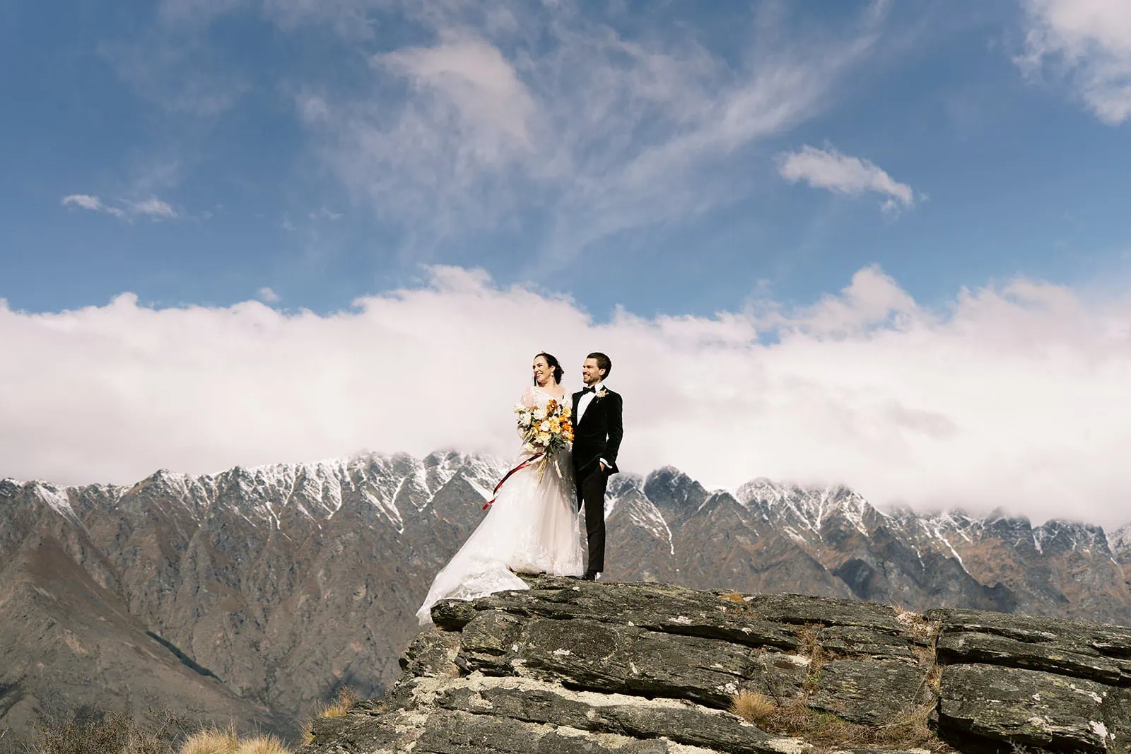 Queenstown Wedding Photographer An EloPement wedding couple standing on top of a cliff in Queenstown, New Zealand.