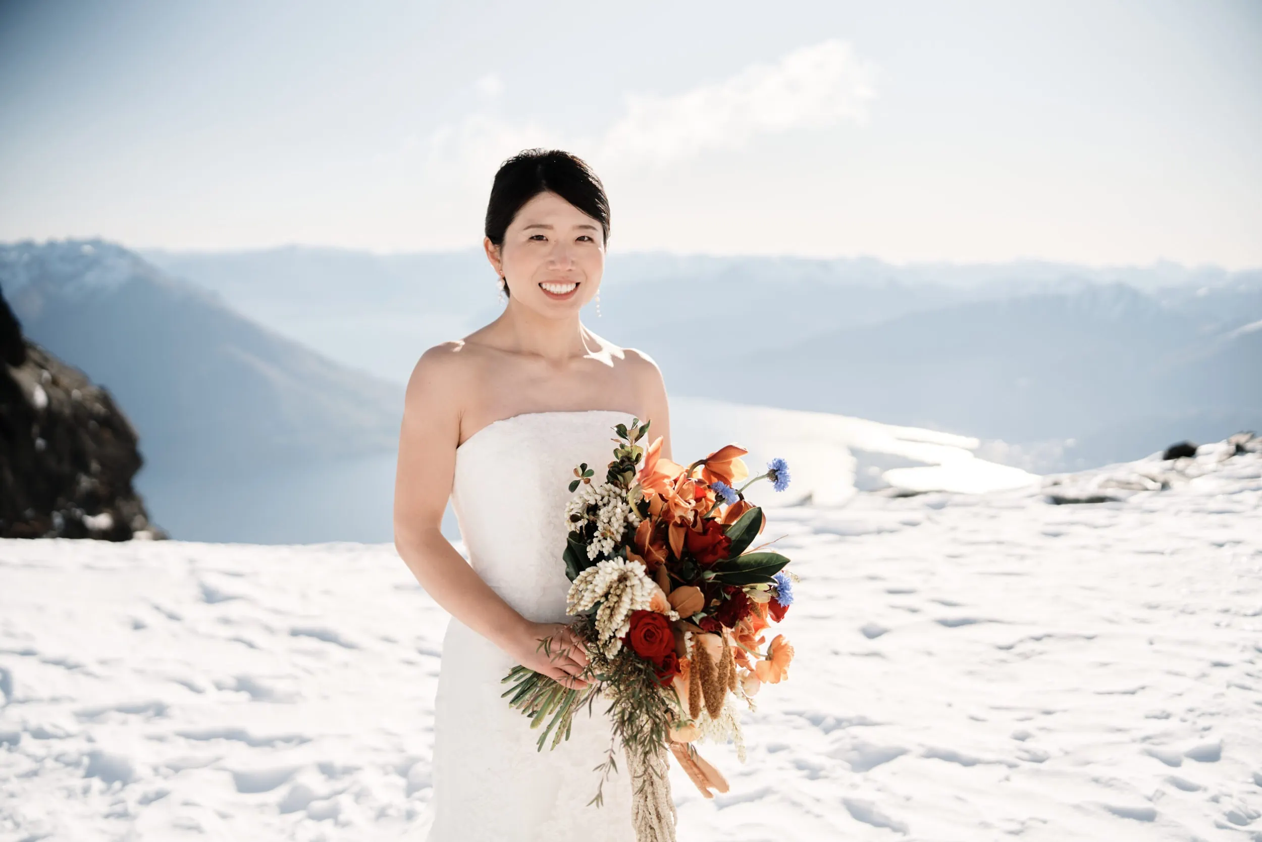 Queenstown Wedding Photographer Asumi & Atsushi's Queenstown Heli Pre Wedding Shoot captures the stunning moment of a bride holding a bouquet on top of a snowy mountain.