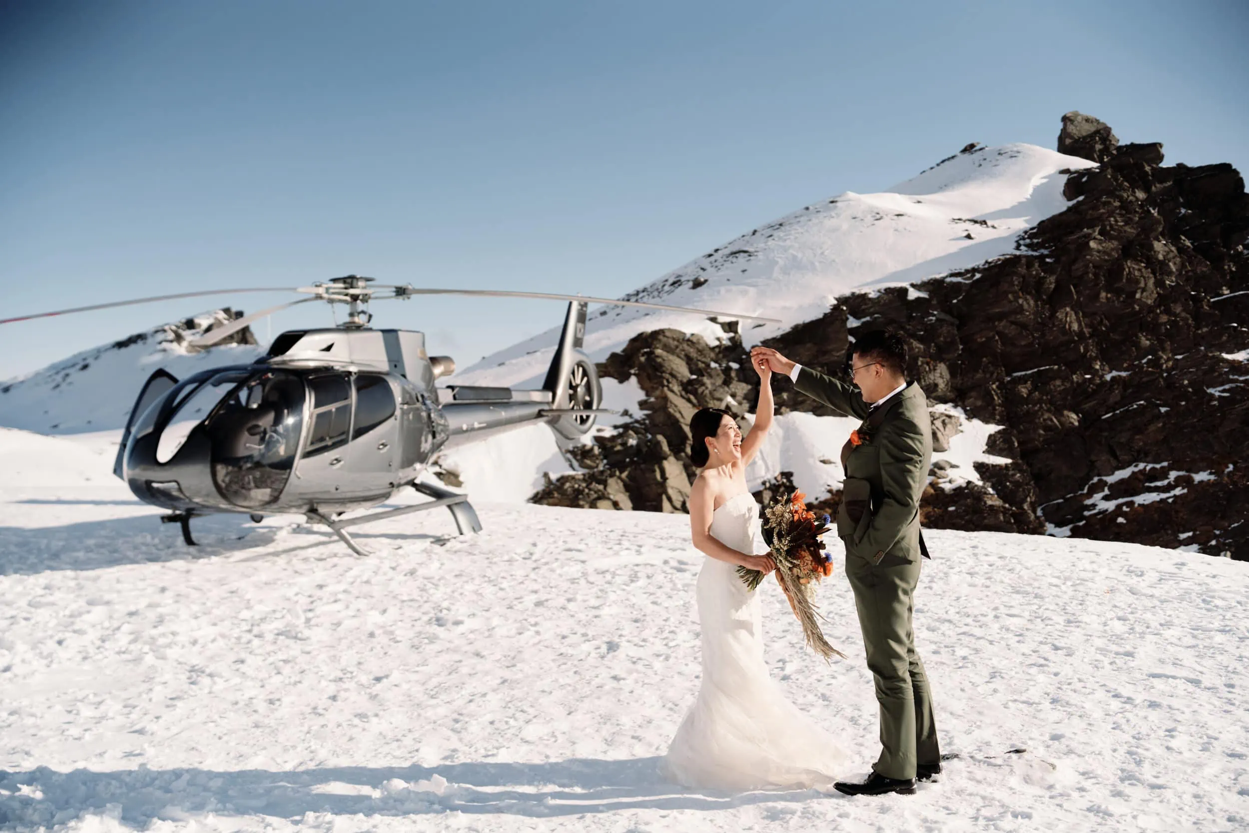 Queenstown Wedding Photographer Asumi and Atsushi, the radiant bride and handsome groom, elegantly pose in front of a helicopter during their breathtaking Queenstown Heli Pre Wedding Shoot.