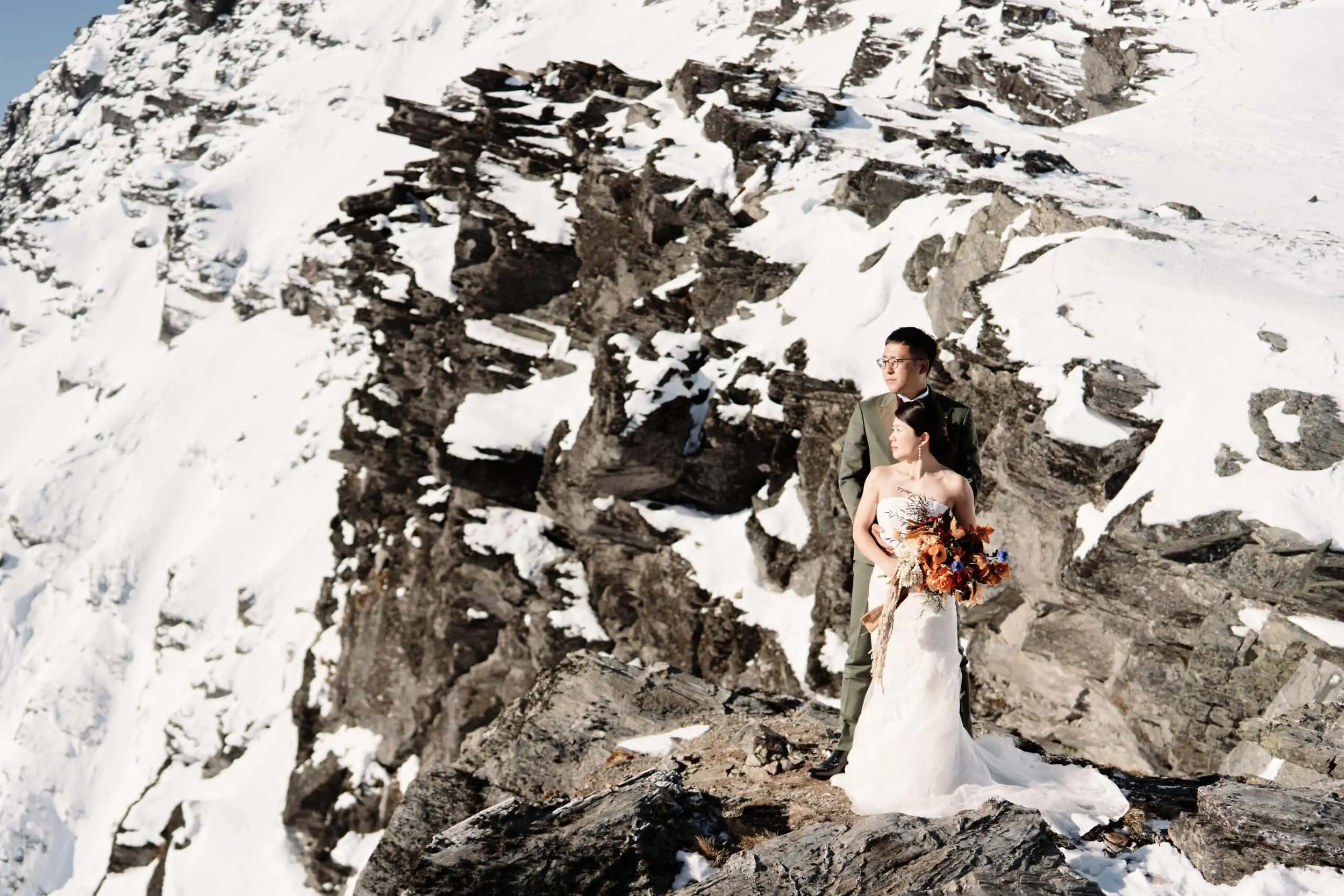 Queenstown Wedding Photographer Atsushi and Asumi, a bride and groom, elegantly pose on top of a picturesque snow-covered mountain during their Queenstown Heli Pre Wedding Shoot.