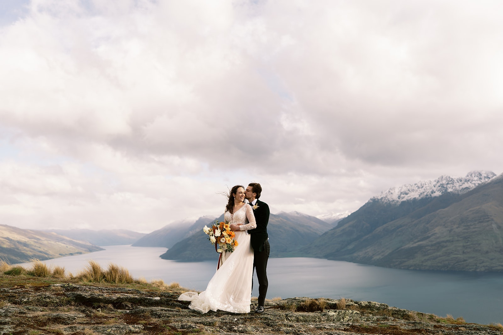Queenstown Wedding Photographer A bride and groom standing on top of a mountain overlooking Lake Wanaka during their EloPement Wedding.