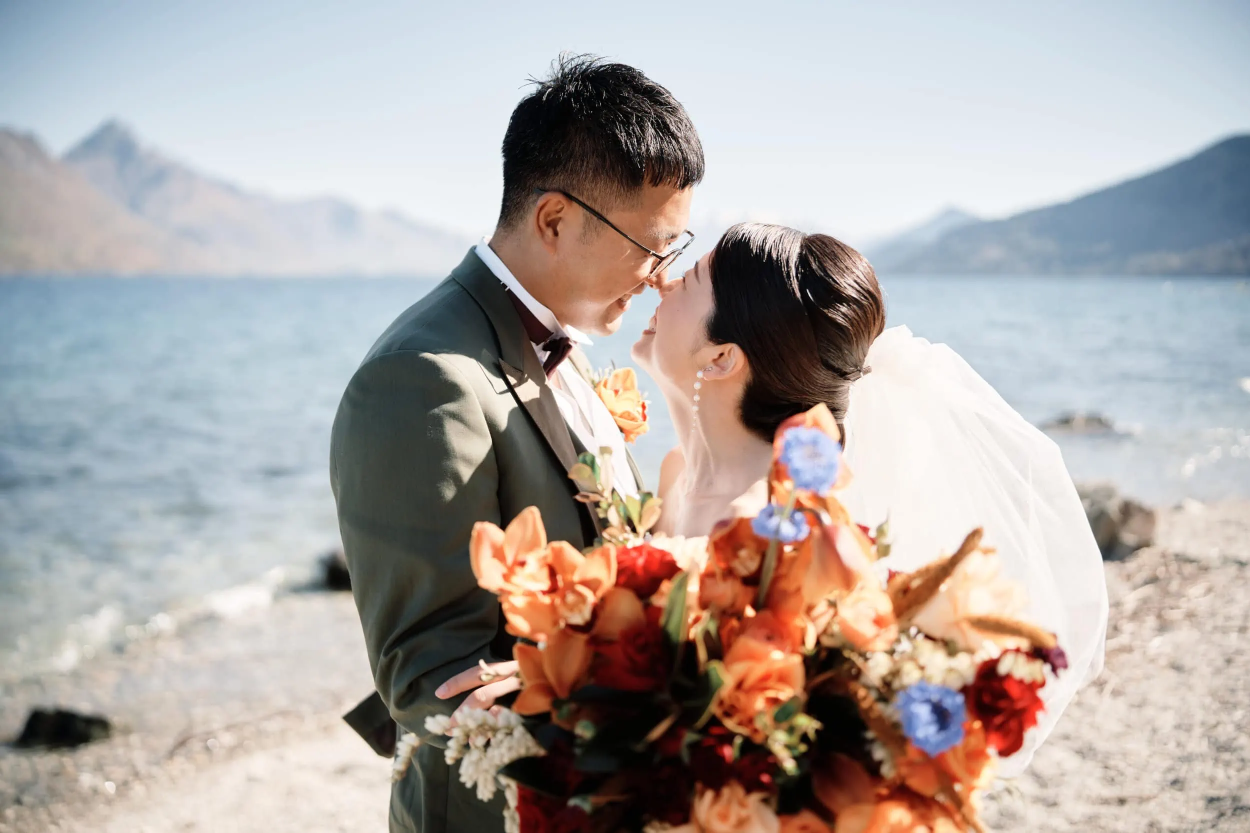 Queenstown Wedding Photographer A bride and groom, Asumi and Atsushi, kissing on the shore of Lake Wanaka near Queenstown.