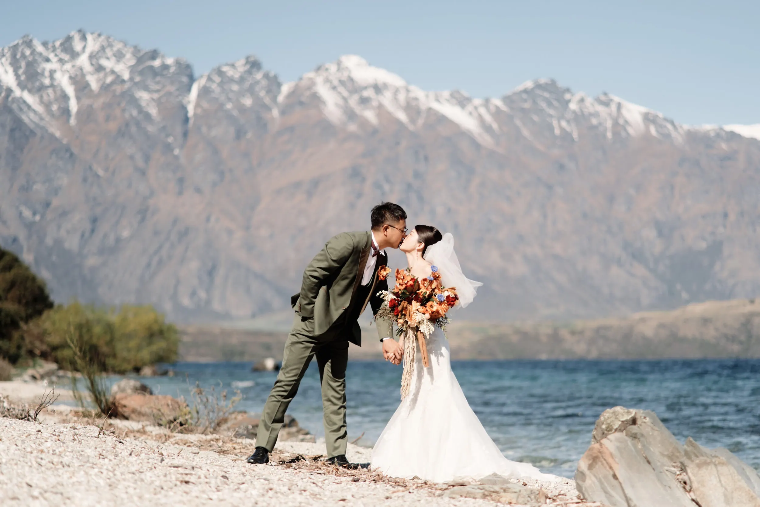 Queenstown Wedding Photographer A bride and groom, Asumi and Atsushi, kiss on the shore of Lake Wanaka in Queenstown.