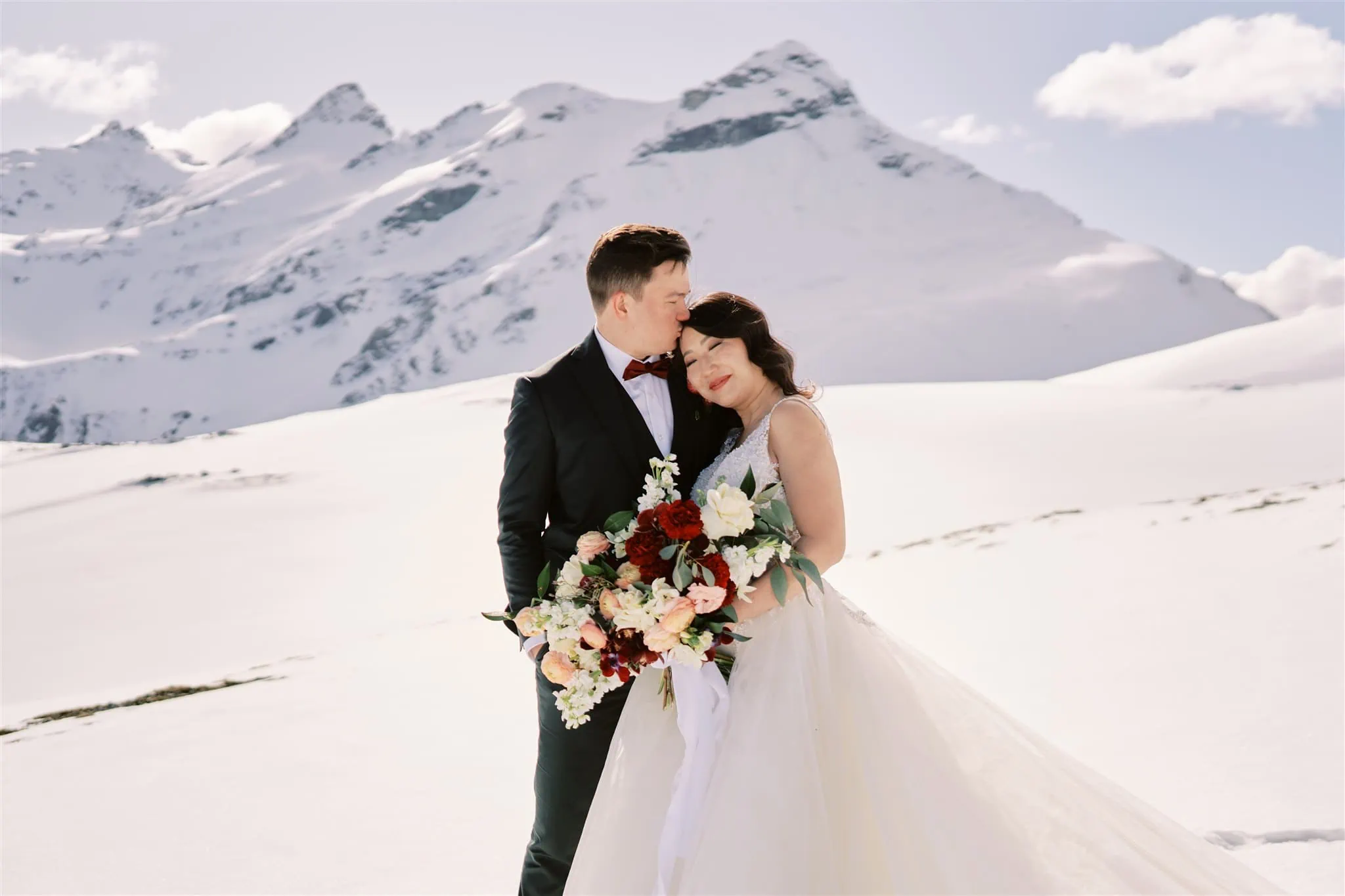 Queenstown Elopement Heli Wedding Photographer クイーンズタウン結婚式 | An elopement wedding with a bride and groom standing in the snow, with mountains in the background.