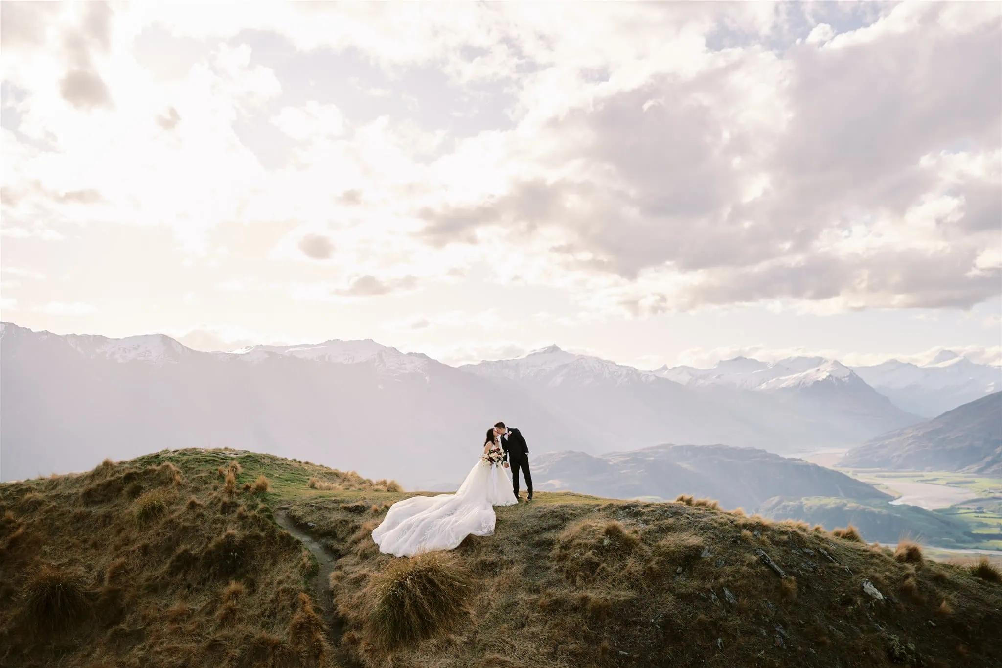 Queenstown Elopement Heli Wedding Photographer クイーンズタウン結婚式 | An elopement wedding couple in a wedding dress on a hill with mountains in the background.