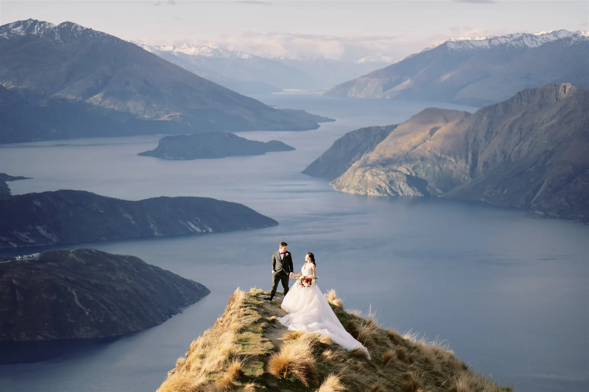 Queenstown Elopement Heli Wedding Photographer クイーンズタウン結婚式 | A man and woman embracing on a cliff overlooking a body of water during their elopement.