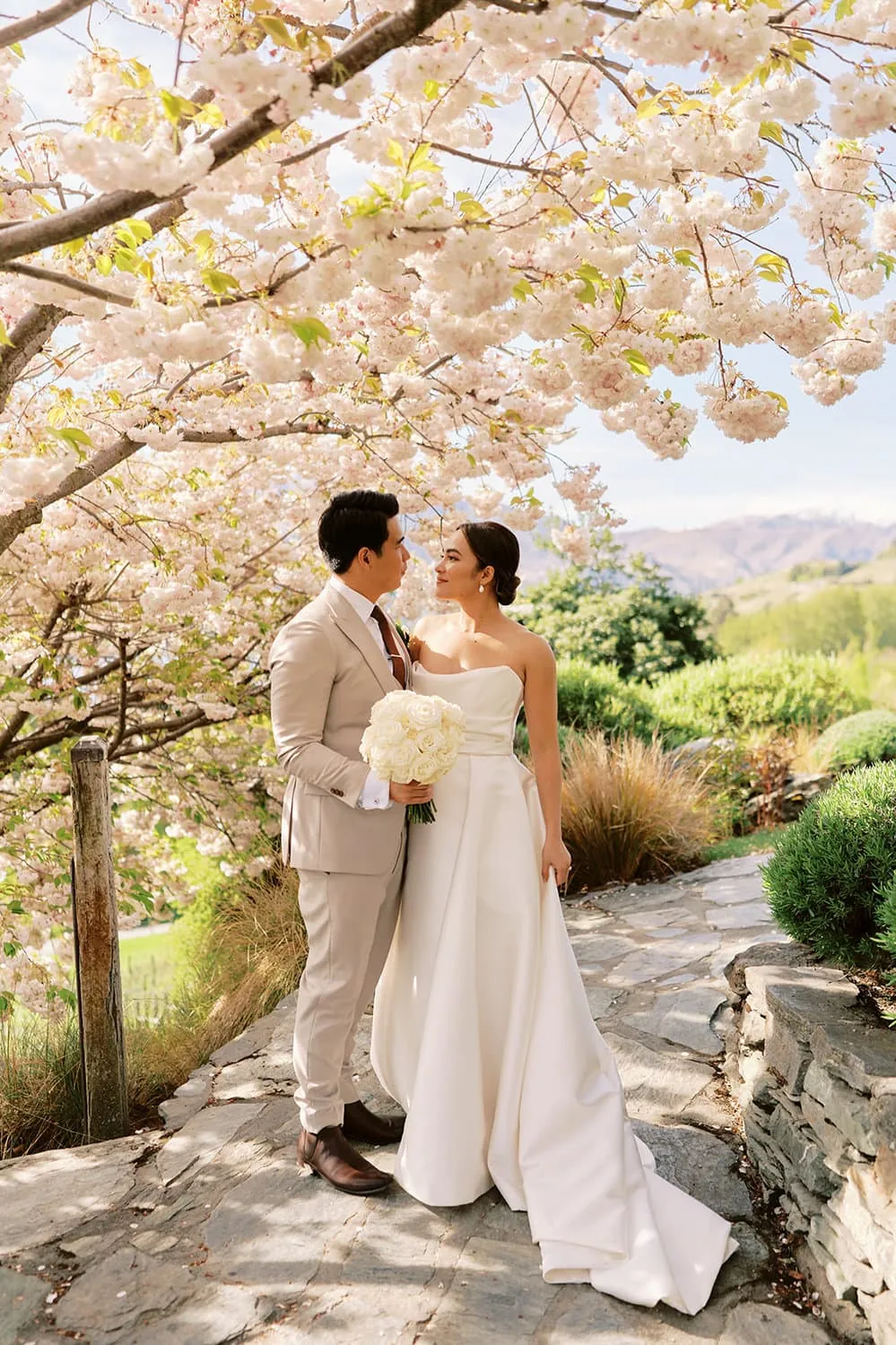 Queenstown Elopement Heli Wedding Photographer クイーンズタウン結婚式 | A bride and groom standing under a cherry blossom tree in Queenstown.