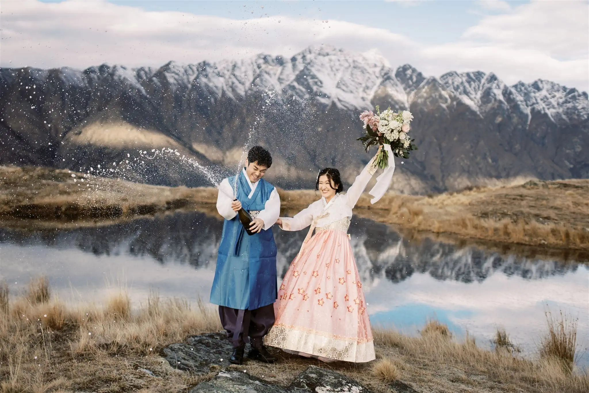 Queenstown Wedding Photographer A bride and groom in traditional Korean attire are standing in front of a lake, enjoying their Queenstown heli-wedding package.