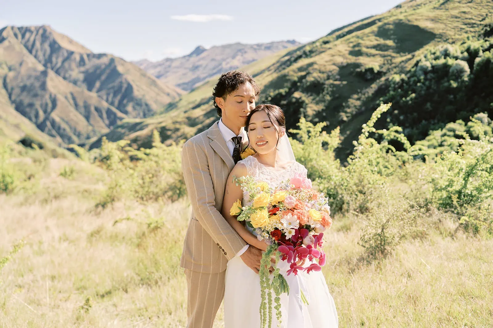 Queenstown Elopement Heli Wedding Photographer クイーンズタウン結婚式 | A Queenstown bride and groom standing in a field with mountains in the background.