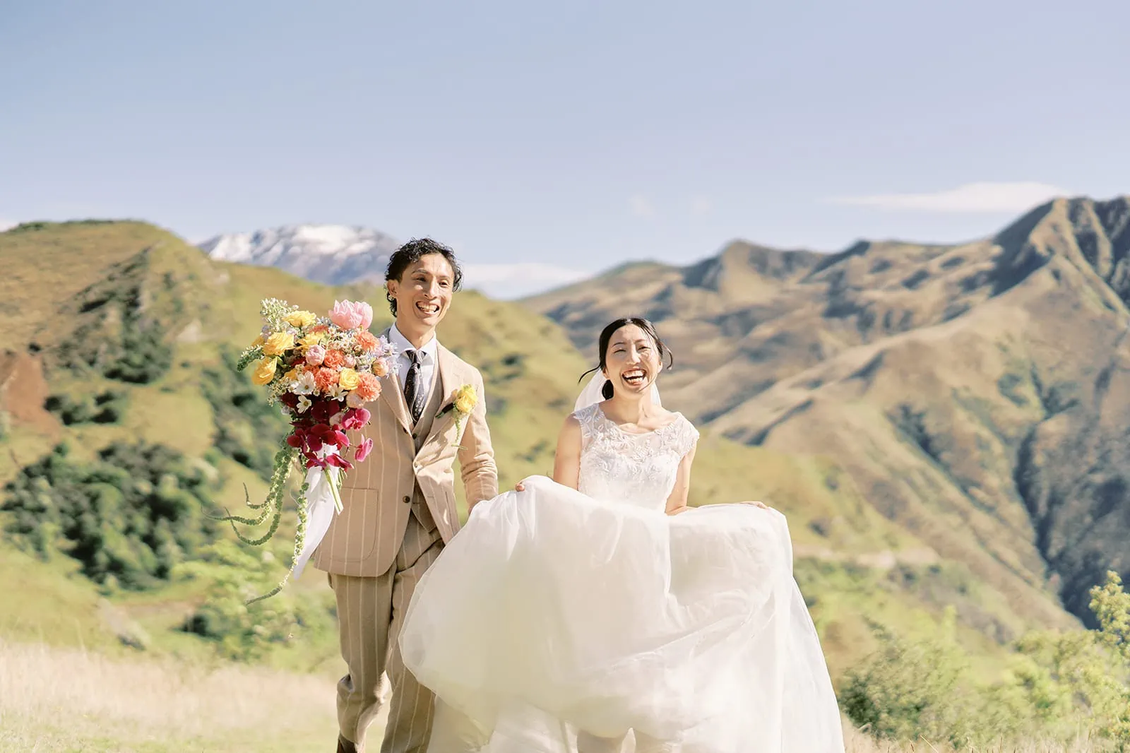 Queenstown Elopement Heli Wedding Photographer クイーンズタウン結婚式 | Taisei and Saki, a bride and groom, walking down a hill with mountains in the background in Queenstown.
