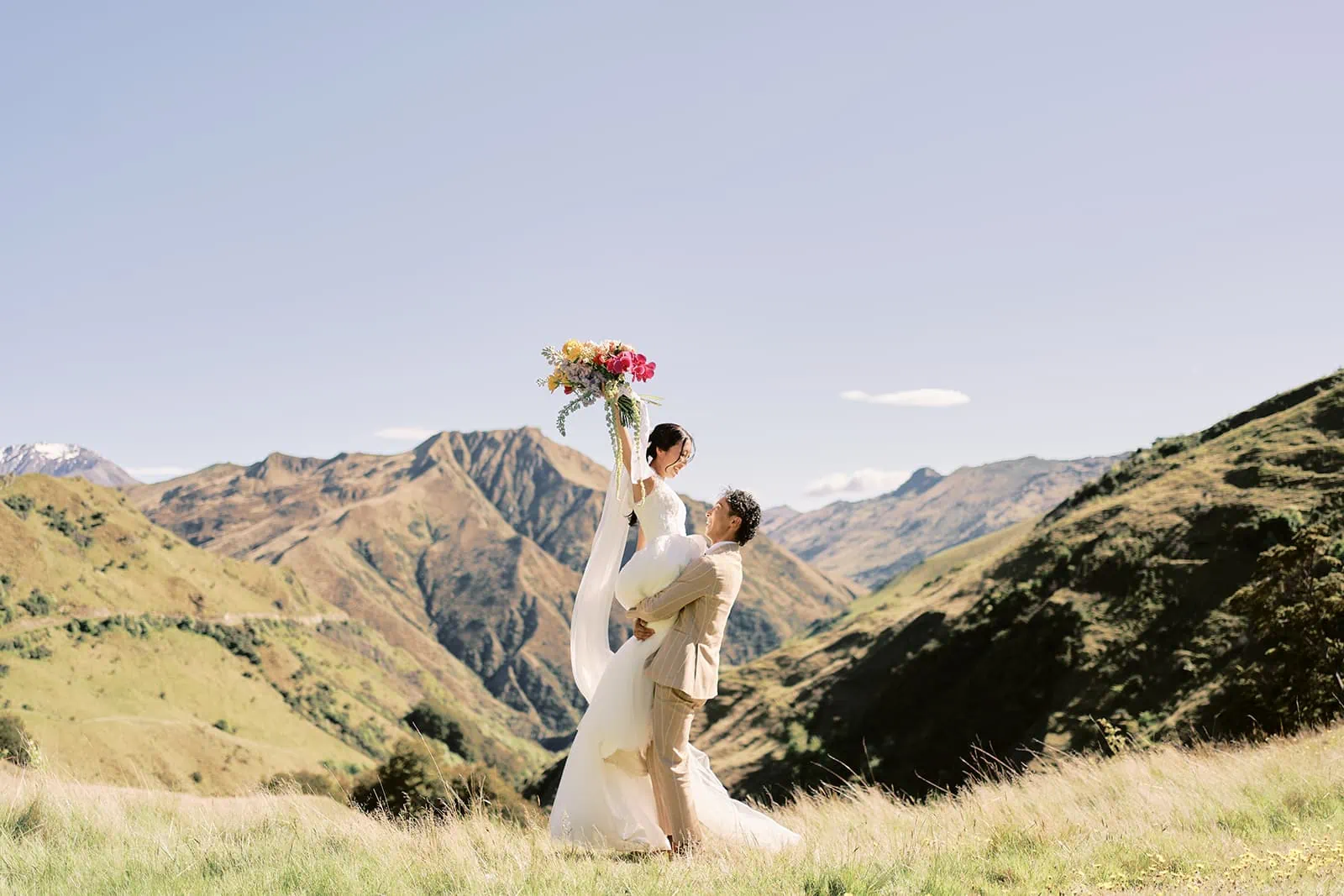 Queenstown Elopement Heli Wedding Photographer クイーンズタウン結婚式 | A Queenstown bride and groom standing on top of a hill in the mountains.