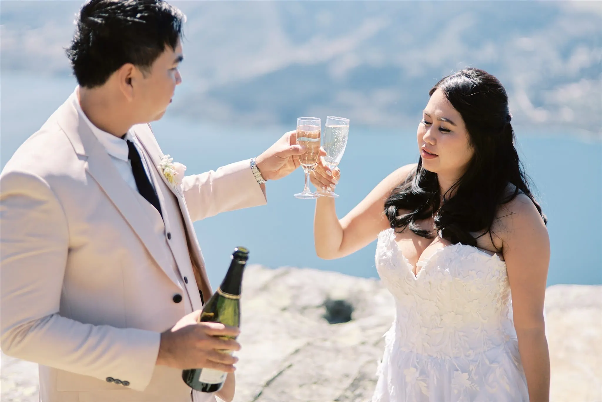 Queenstown Elopement Heli Wedding Photographer クイーンズタウン結婚式 | A Queenstown elopement, with a man and woman holding glasses and standing on a rock.
