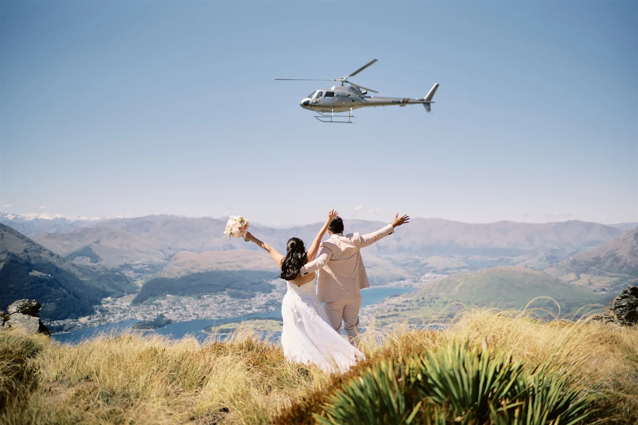 Queenstown Elopement Heli Wedding Photographer クイーンズタウン結婚式 | A Queenstown elopement with a bride and groom standing on a hill, capturing the breathtaking scenery as a helicopter flies in the sky.