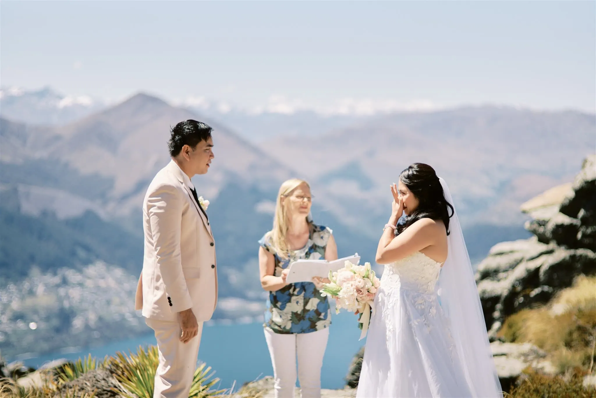 Queenstown Elopement Heli Wedding Photographer クイーンズタウン結婚式 | A man and woman, embraced in love, standing on a cliff overlooking the majestic Queenstown mountains during their intimate elopement ceremony.