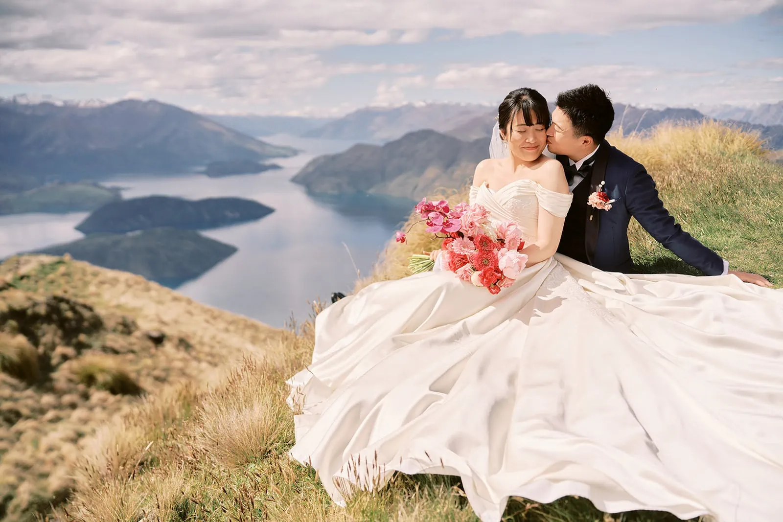 Queenstown Elopement Heli Wedding Photographer クイーンズタウン結婚式 | A pre-wedding photoshoot of a bride and groom sitting on top of a mountain overlooking Lake Wanaka.