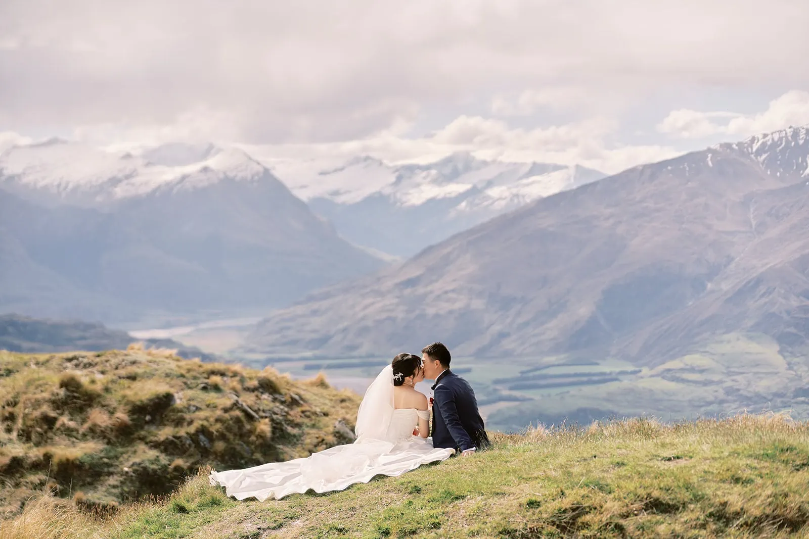 Queenstown Elopement Heli Wedding Photographer クイーンズタウン結婚式 | A couple sitting on a hill overlooking the mountains in New Zealand during their pre-wedding photoshoot.