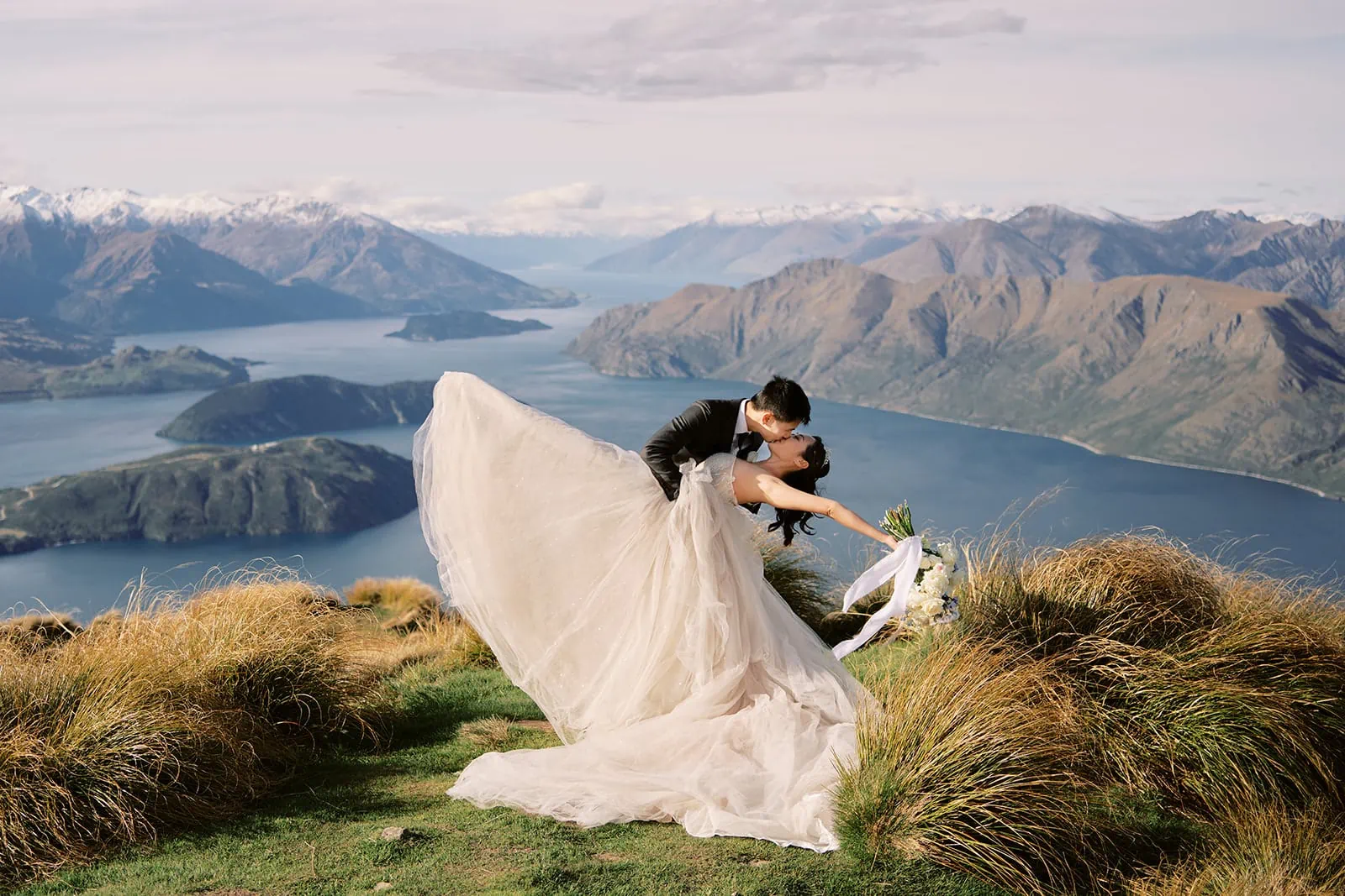 Queenstown Elopement Heli Wedding Photographer クイーンズタウン結婚式 | A bride and groom named Otto and Eusanna kissing on top of a mountain overlooking lake Wanaka.