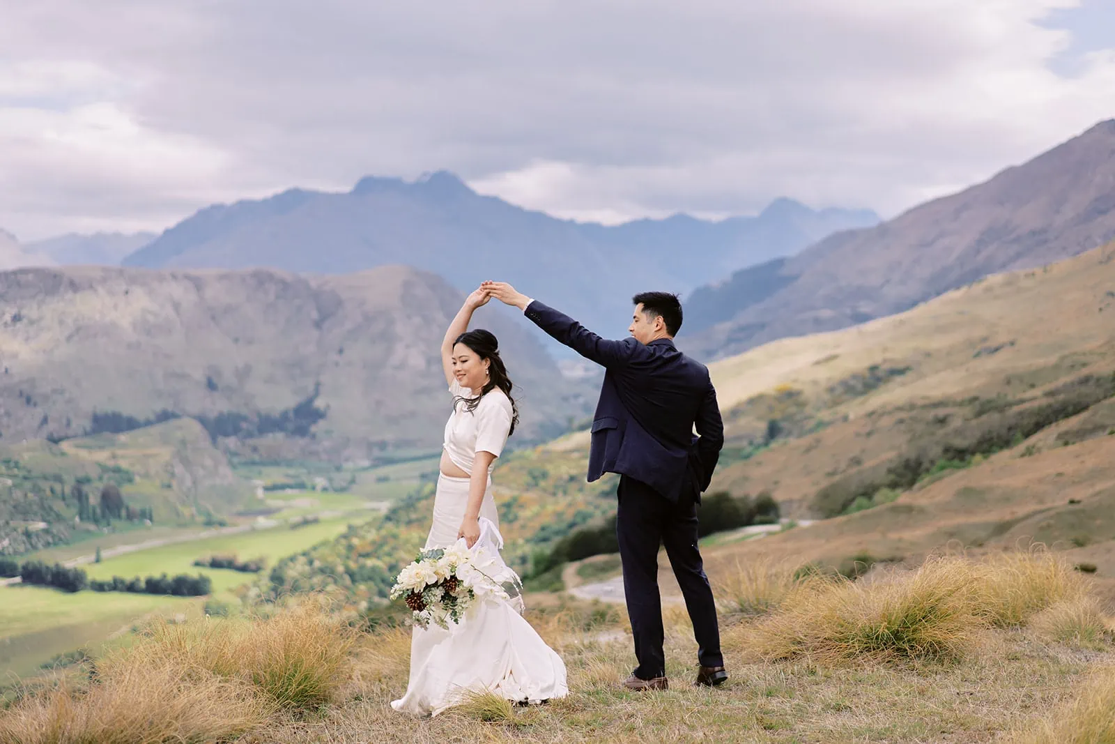Queenstown Elopement Heli Wedding Photographer クイーンズタウン結婚式 | A breathtaking pre-wedding photoshoot of a bride and groom standing on top of a mountain in New Zealand.