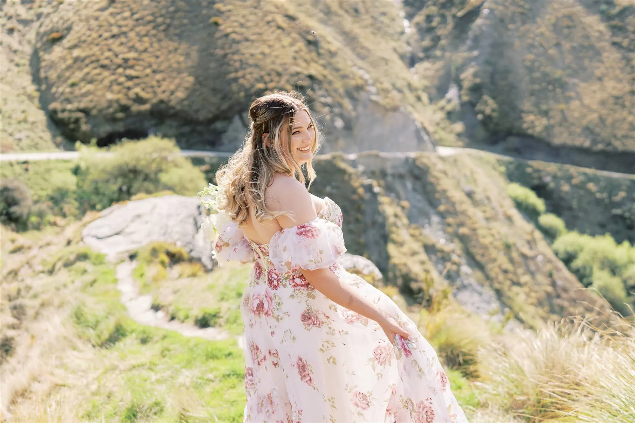 Queenstown Elopement Heli Wedding Photographer クイーンズタウン結婚式 | A woman in a floral dress standing on a hillside in New Zealand for her Coronet Peak elopement.