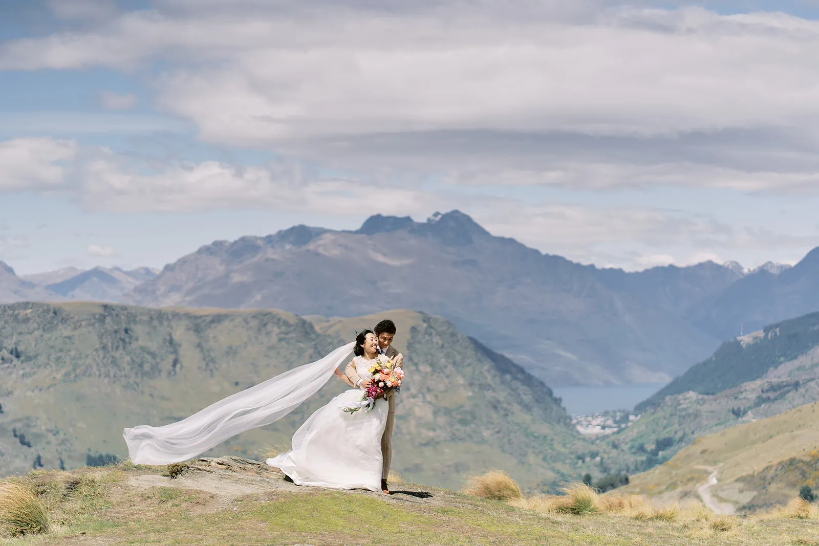 Queenstown Elopement Heli Wedding Photographer クイーンズタウン結婚式 | Saki & Taisei's Queenstown Heli Pre-Wedding Photoshoot captures a breathtaking moment of the bride standing on top of a hill with majestic mountains in the background.