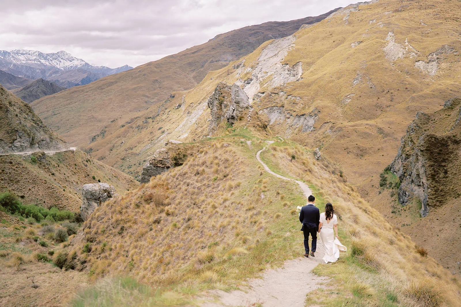 Queenstown Elopement Heli Wedding Photographer クイーンズタウン結婚式 | A man and woman, in their pre-wedding photoshoot, walking on a path in a mountain.
