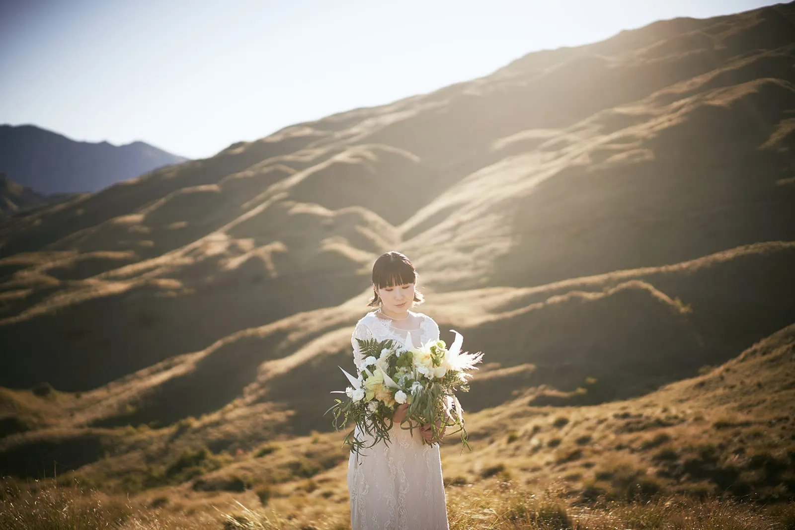 Queenstown Elopement Heli Wedding Photographer クイーンズタウン結婚式 | Queenstown Heli Pre-Wedding Shoot featuring Eriko & Naoki, with a bride in a white dress standing in the middle of a mountain.