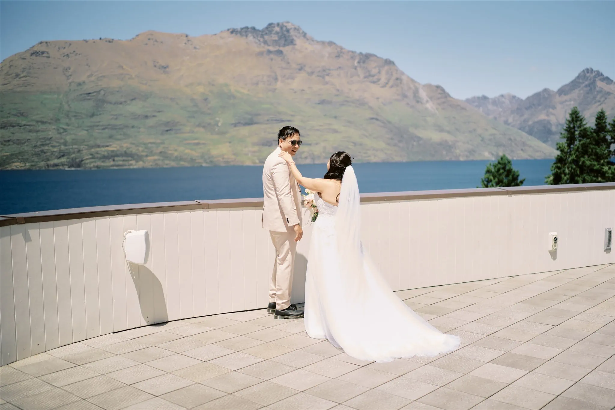 Queenstown Elopement Heli Wedding Photographer クイーンズタウン結婚式 | A man and woman embracing on a terrace in Queenstown with mountains in the background during their elopement ceremony.