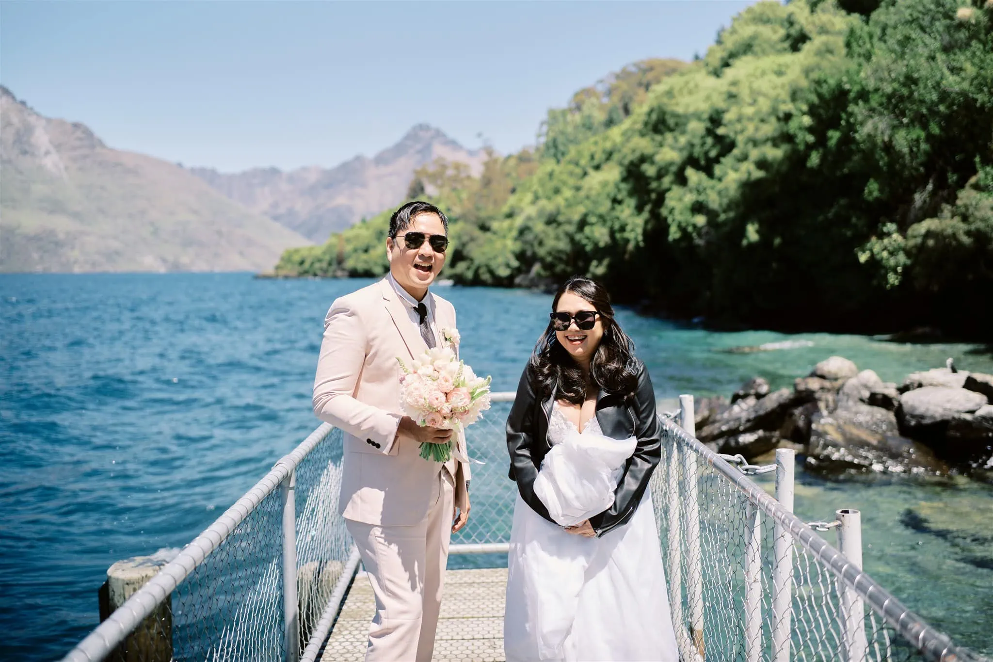 Queenstown Elopement Heli Wedding Photographer クイーンズタウン結婚式 | A Queenstown elopement - a bride and groom standing on a dock in front of a lake.