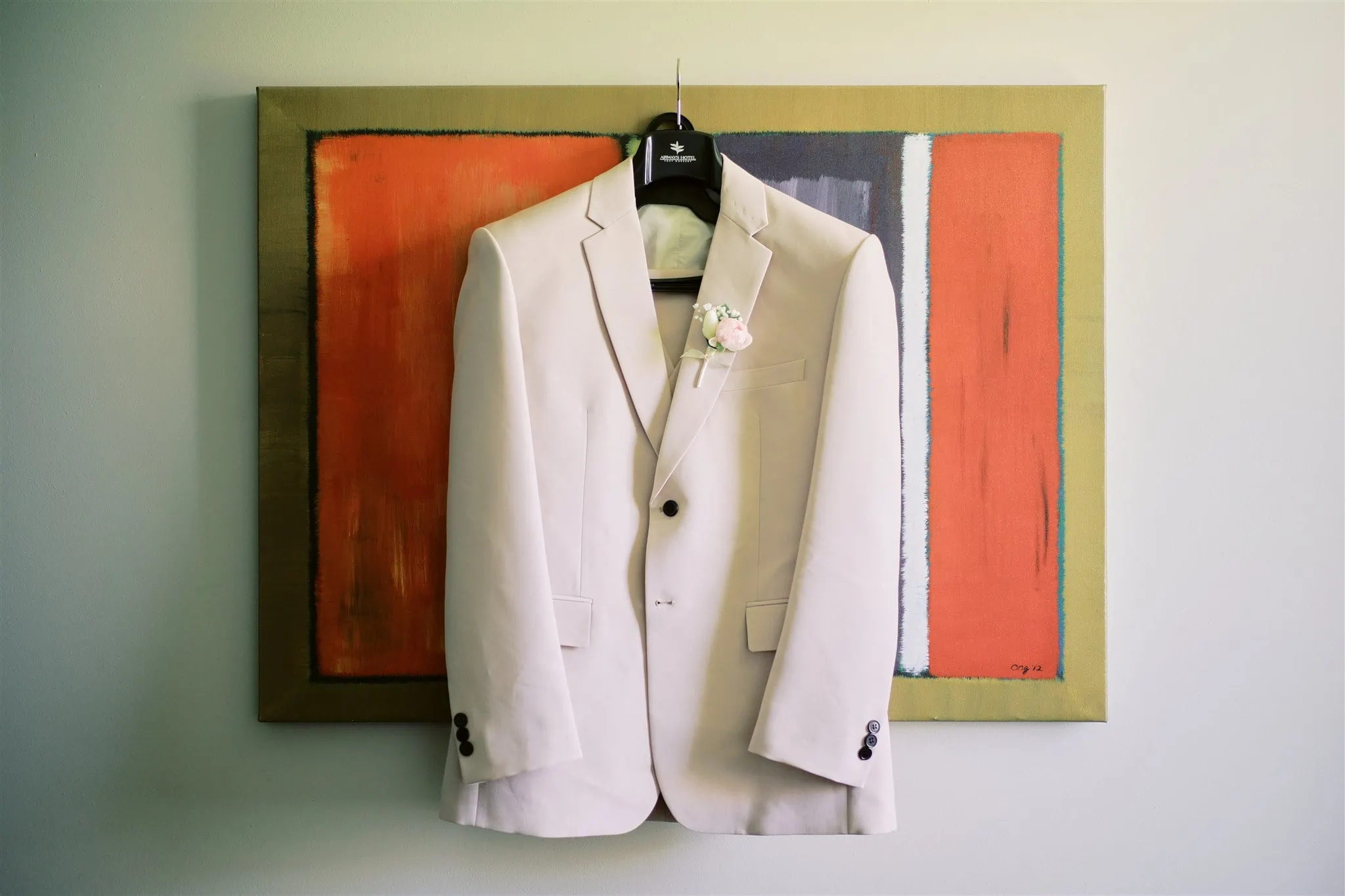 Queenstown Elopement Heli Wedding Photographer クイーンズタウン結婚式 | A white suit, fitting for a Queenstown elopement, hangs on a wall next to a painting.