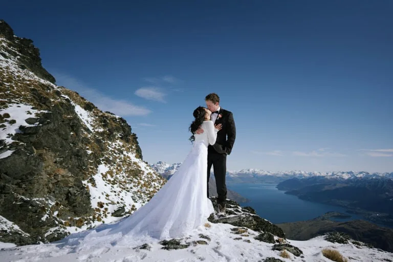 Queenstown Elopement Heli Wedding Photographer クイーンズタウン結婚式 | Kim and Matthew, a man and woman, sharing a passionate kiss on a snowy mountain in Queenstown.