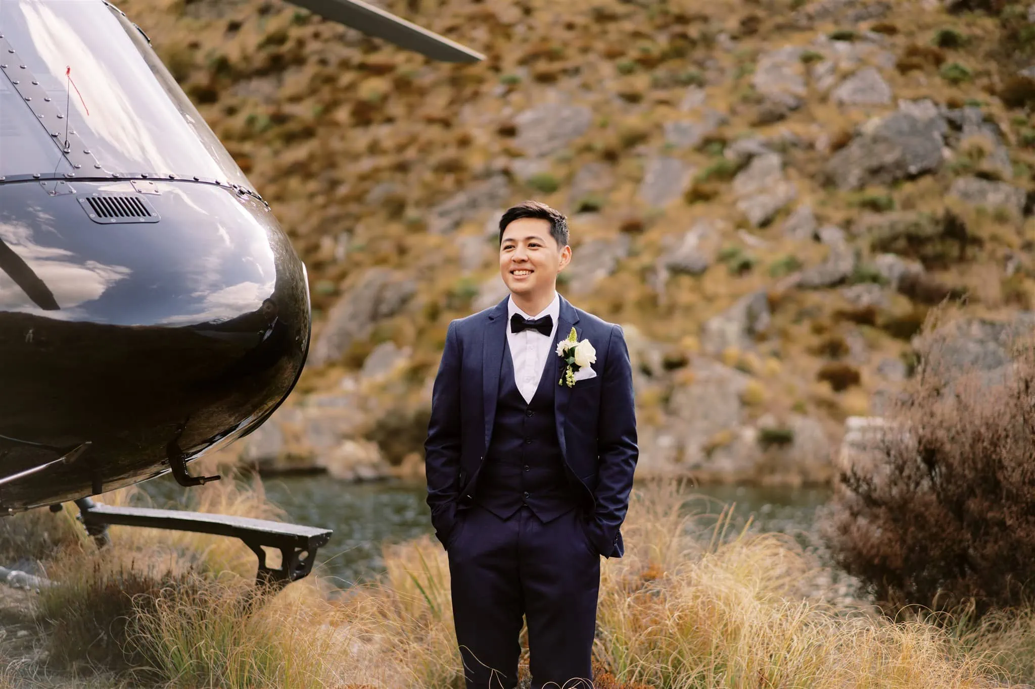 Queenstown Elopement Heli Wedding Photographer クイーンズタウン結婚式 | A man in a tuxedo standing next to a helicopter in Queenstown.