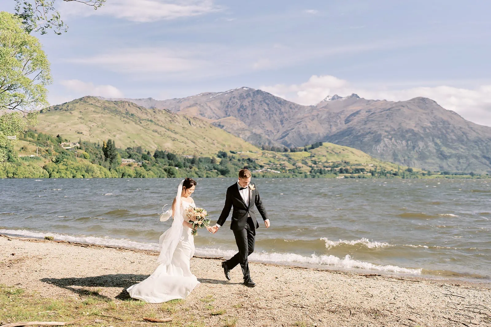 Queenstown Elopement Heli Wedding Photographer クイーンズタウン結婚式 | Mj and Shane, a bride and groom, walking along the shore of Lake Wanaka near Stoneridge.