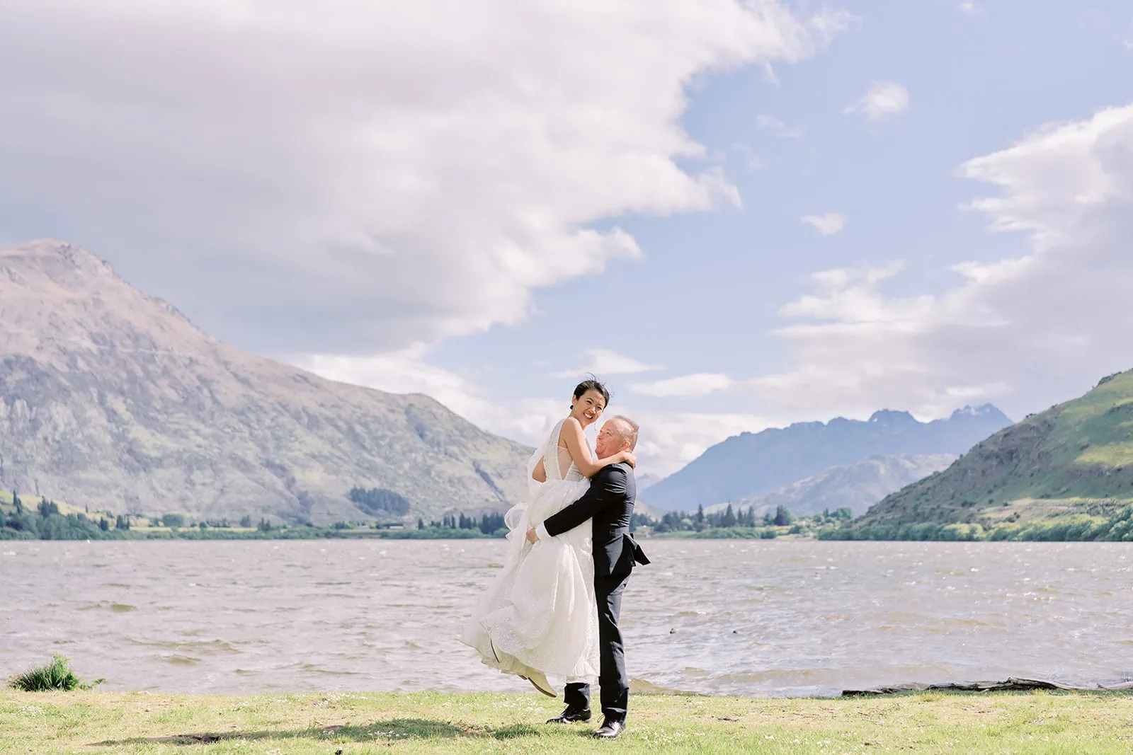 Queenstown Elopement Heli Wedding Photographer クイーンズタウン結婚式 | Meng & Joel, a bride and groom, exchange vows in front of a picturesque lake at Stoneridge Estate during their New Zealand wedding.