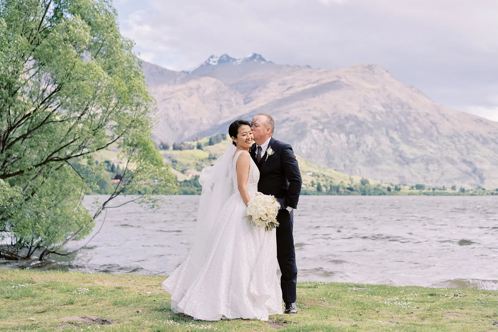 Queenstown Elopement Heli Wedding Photographer クイーンズタウン結婚式 | Joel and Meng, the bride and groom, blissfully stand in front of Stoneridge Estate, with a magnificent lake and majestic mountains as their enchanting backdrop.