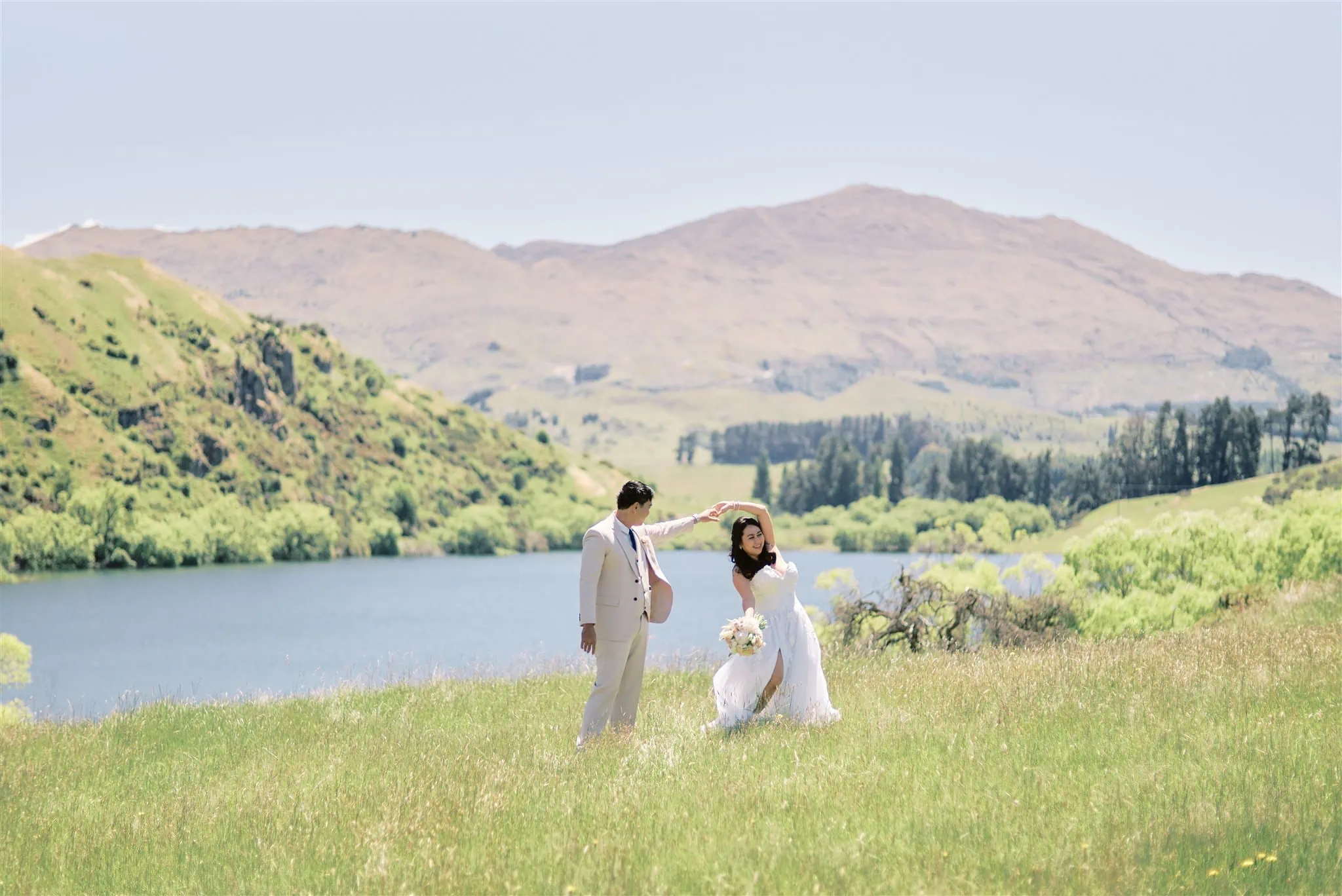 Queenstown Elopement Heli Wedding Photographer クイーンズタウン結婚式 | A man and woman having a romantic Queenstown elopement in a field with majestic mountains in the background.