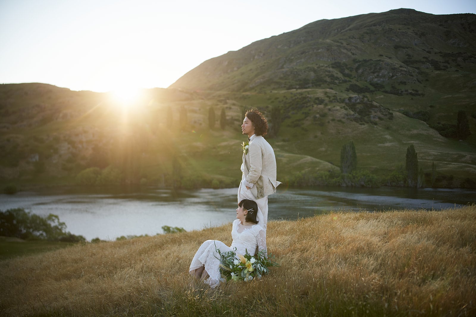 Queenstown Elopement Heli Wedding Photographer クイーンズタウン結婚式 | Eriko & Naoki, a bride and groom, having their Pre-Wedding Shoot in a grassy field at sunset with the stunning backdrop of Queenstown Heli.