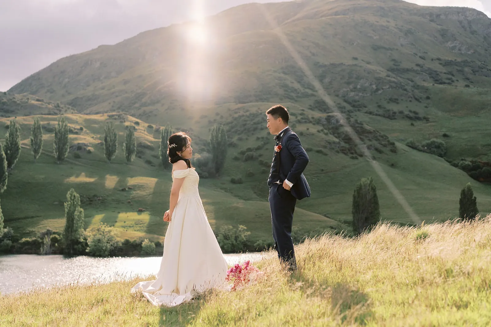 Queenstown Elopement Heli Wedding Photographer クイーンズタウン結婚式 | A bride and groom having a pre-wedding photoshoot on a hill overlooking a lake.