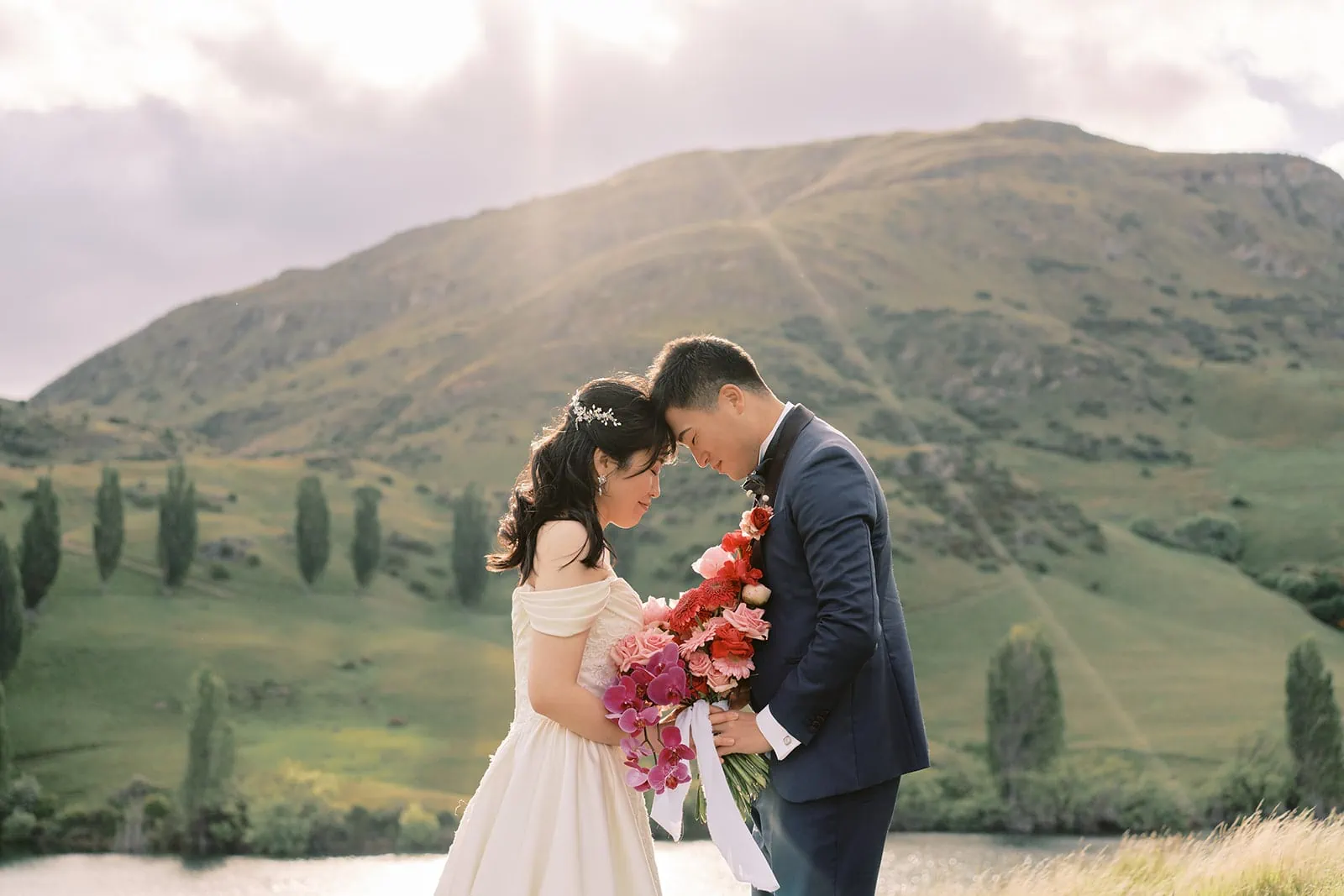 Queenstown Elopement Heli Wedding Photographer クイーンズタウン結婚式 | A picturesque pre-wedding photoshoot captures a bride and groom exquisitely posed in front of a serene lake framed by majestic mountains.