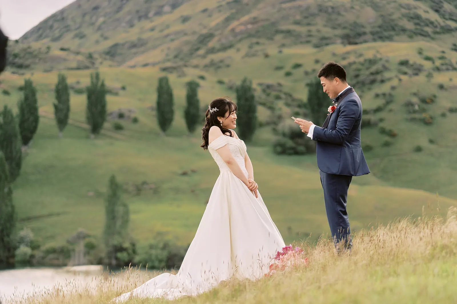 Queenstown Elopement Heli Wedding Photographer クイーンズタウン結婚式 | A pre-wedding photoshoot featuring a bride and groom standing in a field, with majestic mountains as the breathtaking backdrop.