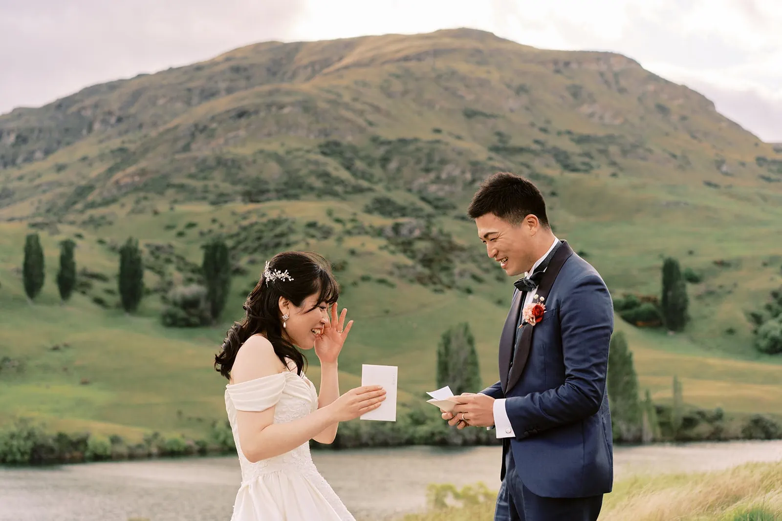 Queenstown Elopement Heli Wedding Photographer クイーンズタウン結婚式 | Pre-wedding photoshoot of a bride and groom in front of a picturesque lake nestled amidst majestic mountains.