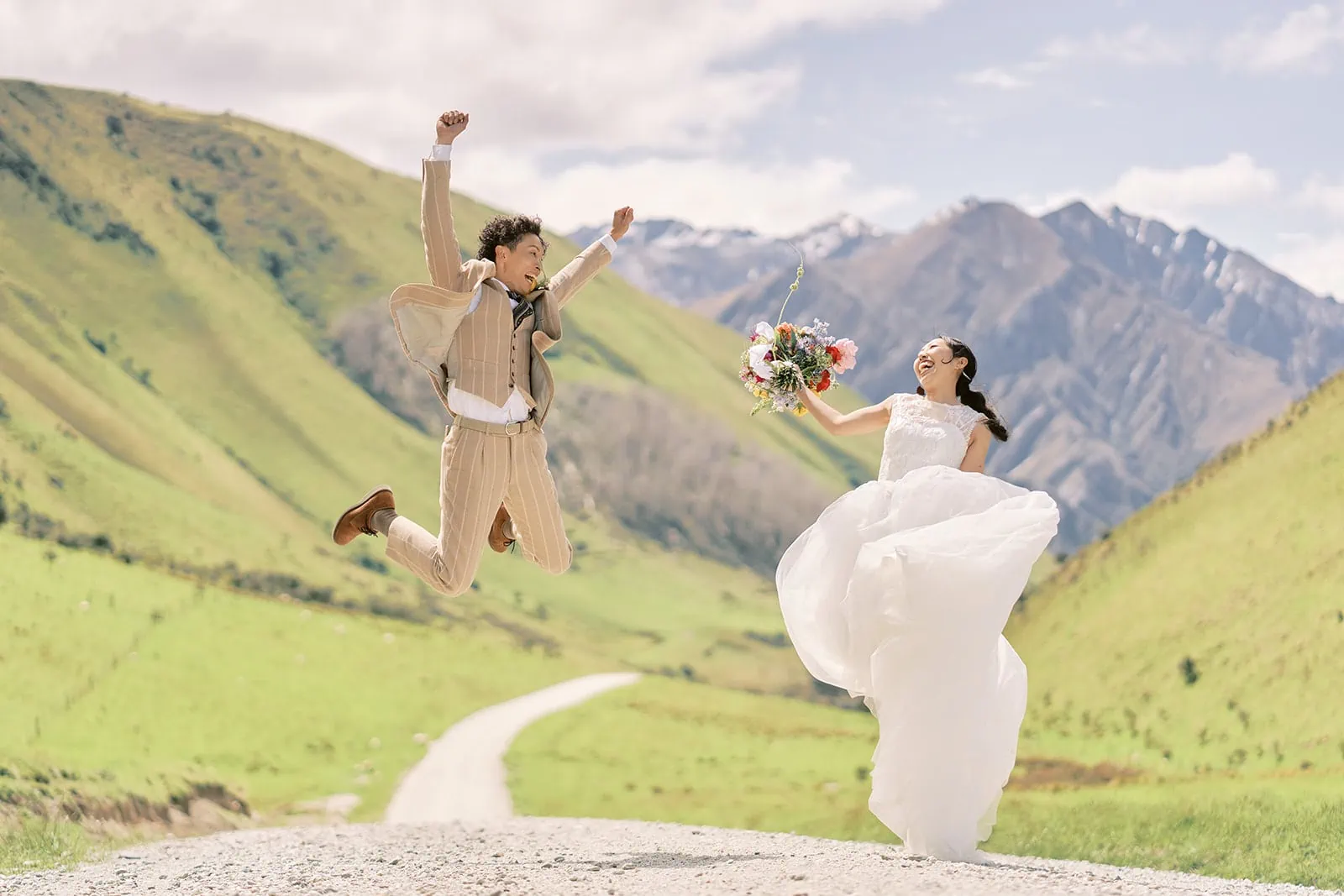Queenstown Elopement Heli Wedding Photographer クイーンズタウン結婚式 | A Saki bride and Taisei groom jumping in the air on a road in Queenstown's majestic mountains.
