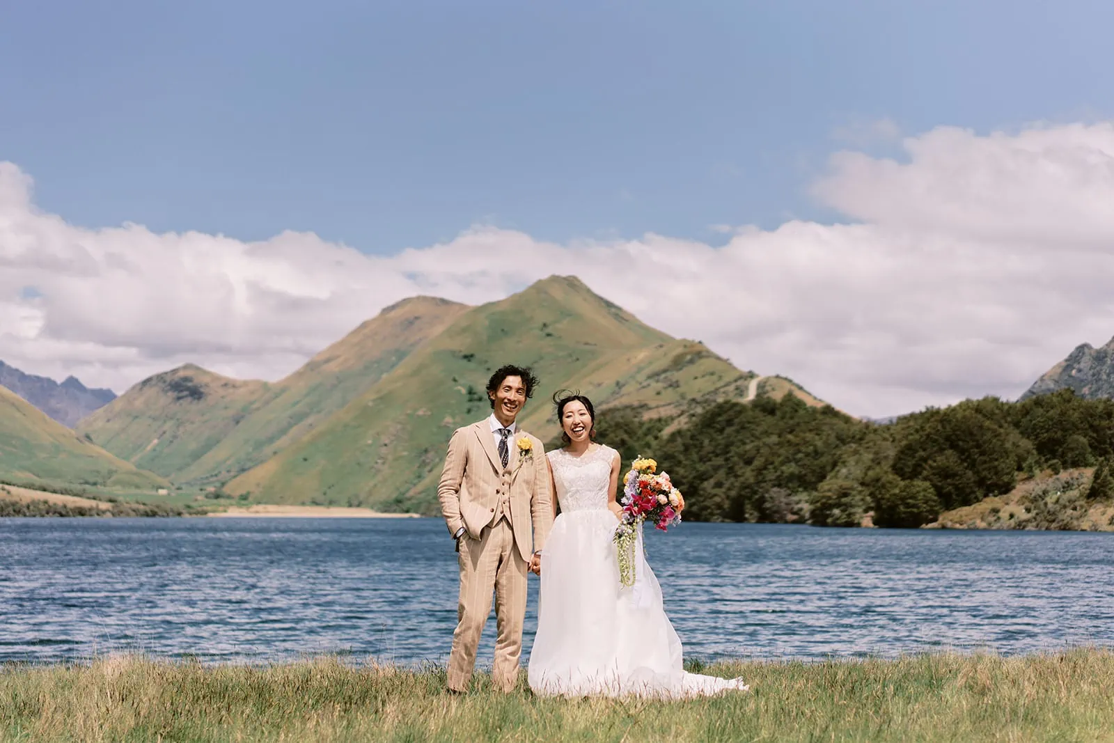 Queenstown Elopement Heli Wedding Photographer クイーンズタウン結婚式 | A bride and groom standing in front of a lake in Queenstown, New Zealand.