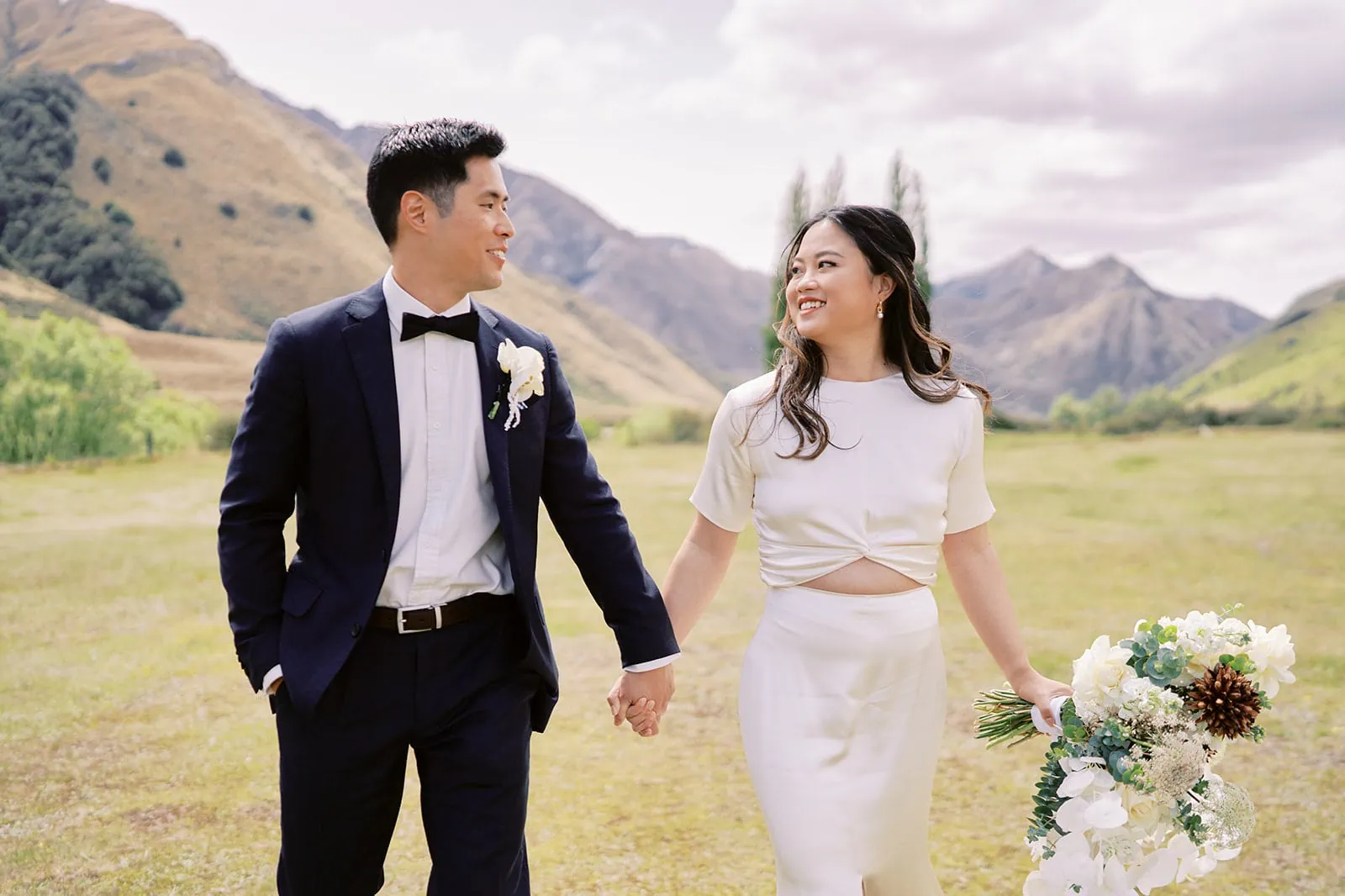 Queenstown Elopement Heli Wedding Photographer クイーンズタウン結婚式 | A couple having their pre-wedding photoshoot, holding hands and walking in a field.