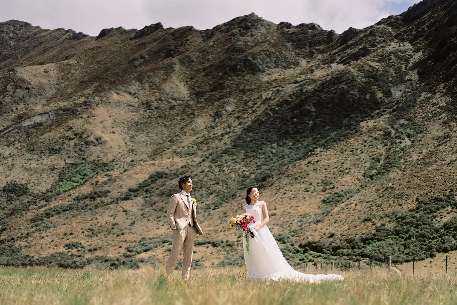 Queenstown Elopement Heli Wedding Photographer クイーンズタウン結婚式 | Saki and Taisei, a bride and groom, standing in a field with mountains in the background near Queenstown.