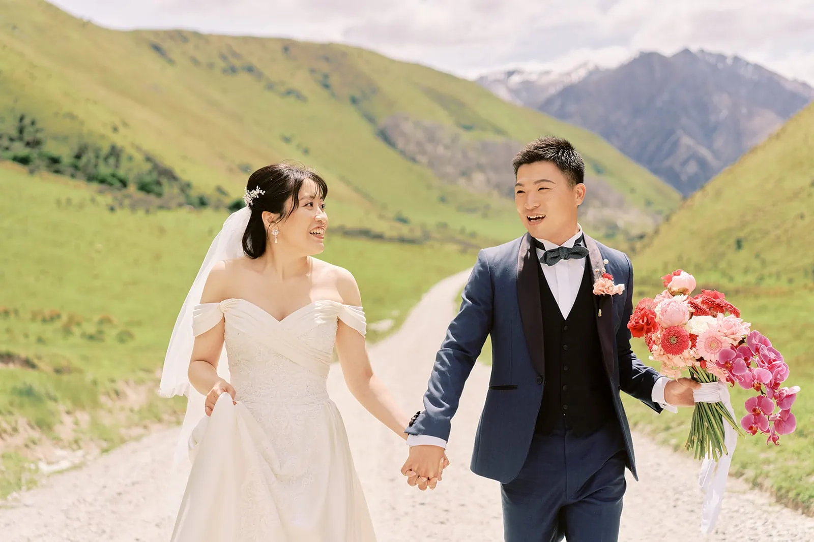 Queenstown Elopement Heli Wedding Photographer クイーンズタウン結婚式 | A couple on a pre-wedding photoshoot, holding hands and blissfully walking on a path with majestic mountains in the background.